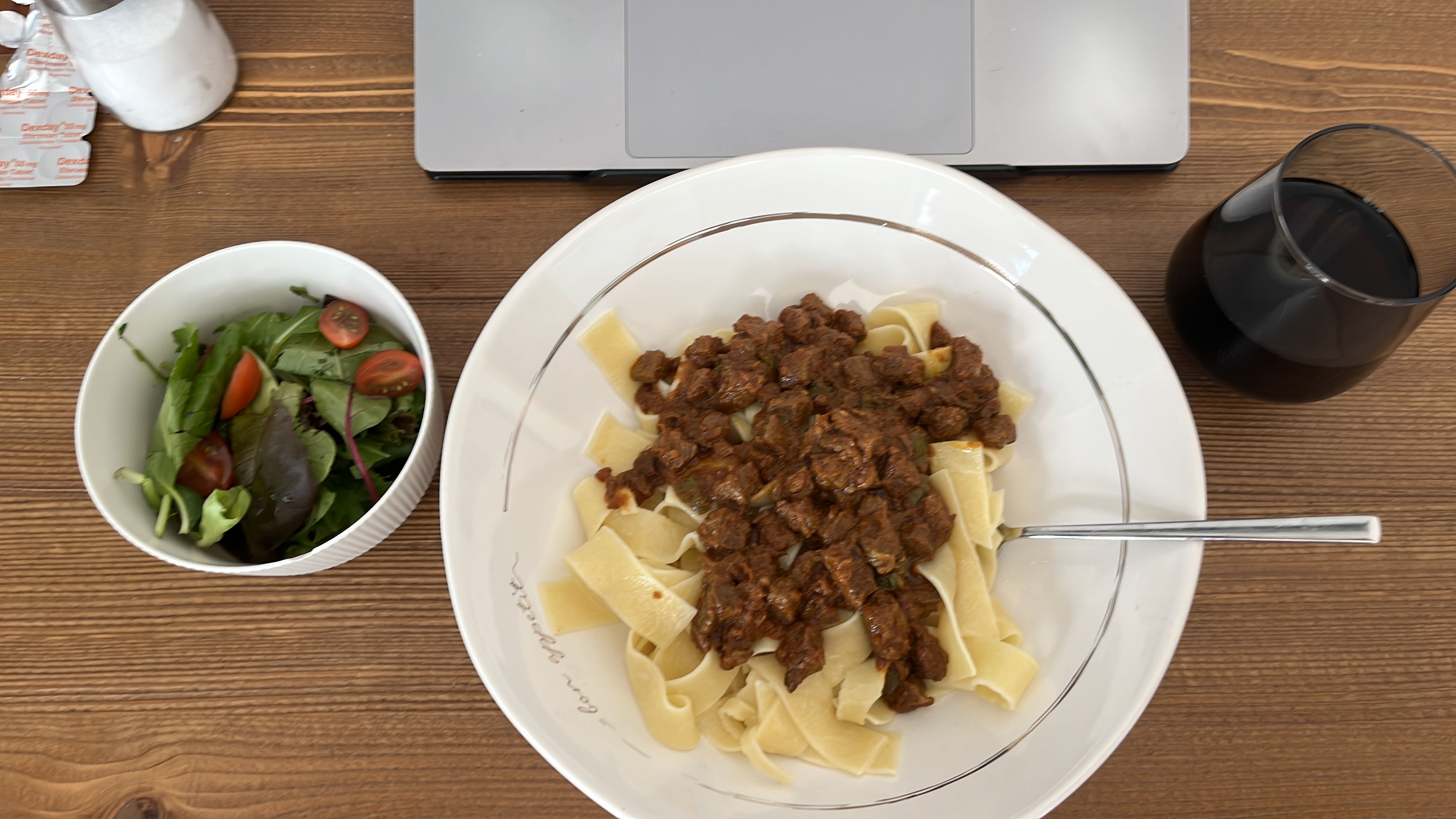 A meal consisting of pasta with beef stew and a side salad, accompanied by a glass of red wine.