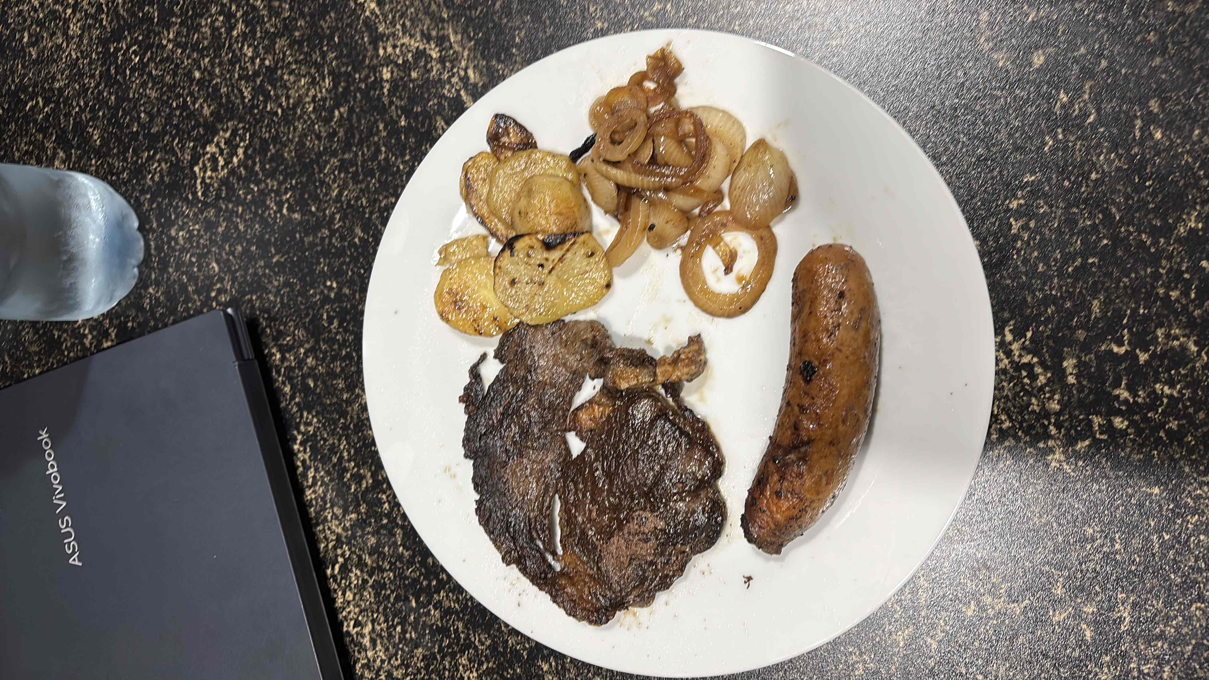 A plate containing grilled steak, sausage, potatoes, and onions, providing a balanced mix of protein, fats, and carbs.