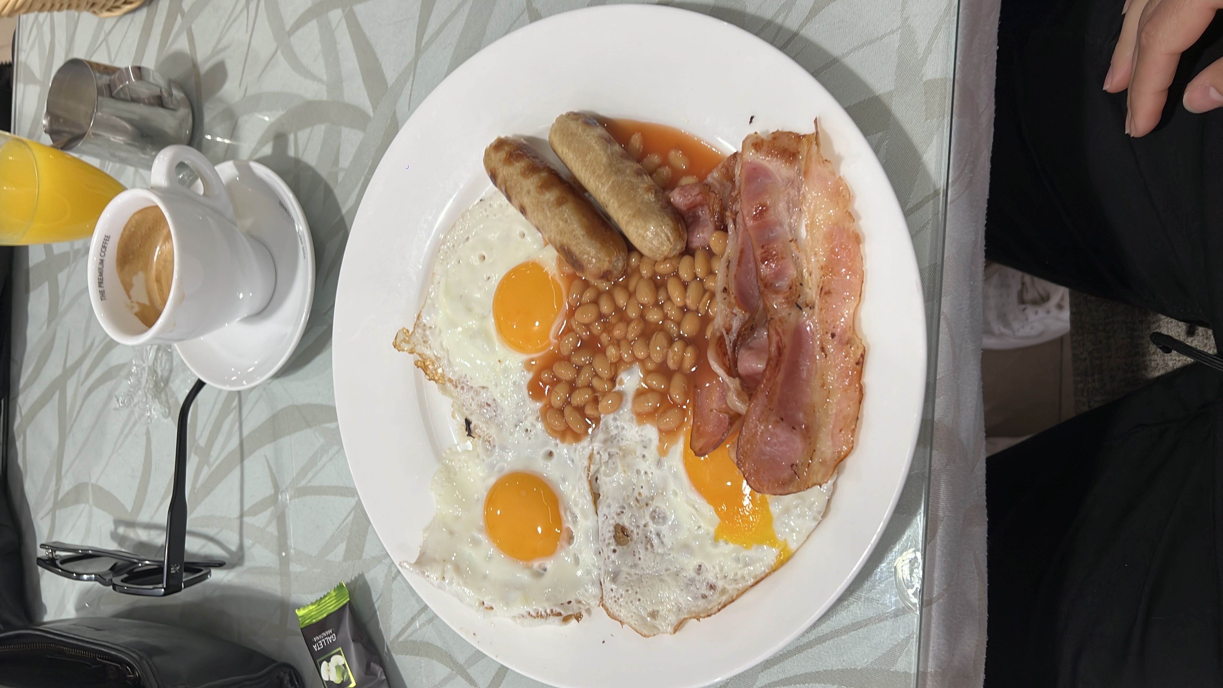 A traditional breakfast plate featuring eggs, bacon, sausages, baked beans, and a glass of orange juice.