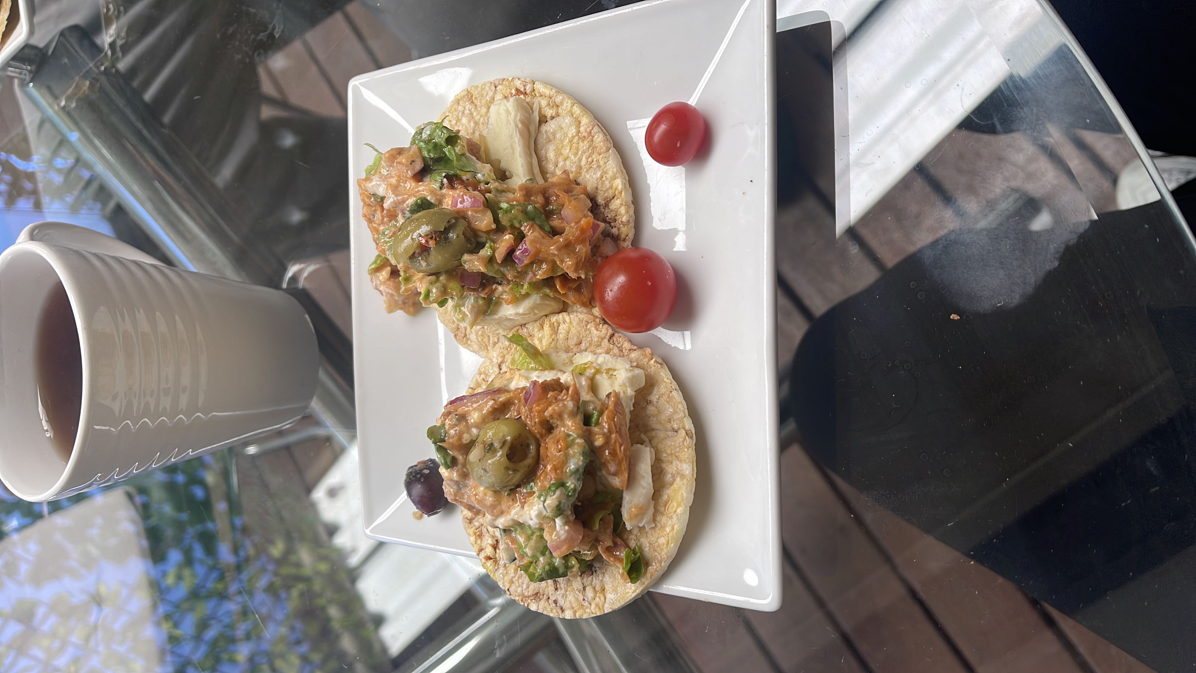 A light meal consisting of rice cakes topped with tuna salad, lettuce, olives, and cherry tomatoes, served with a cup of tea.