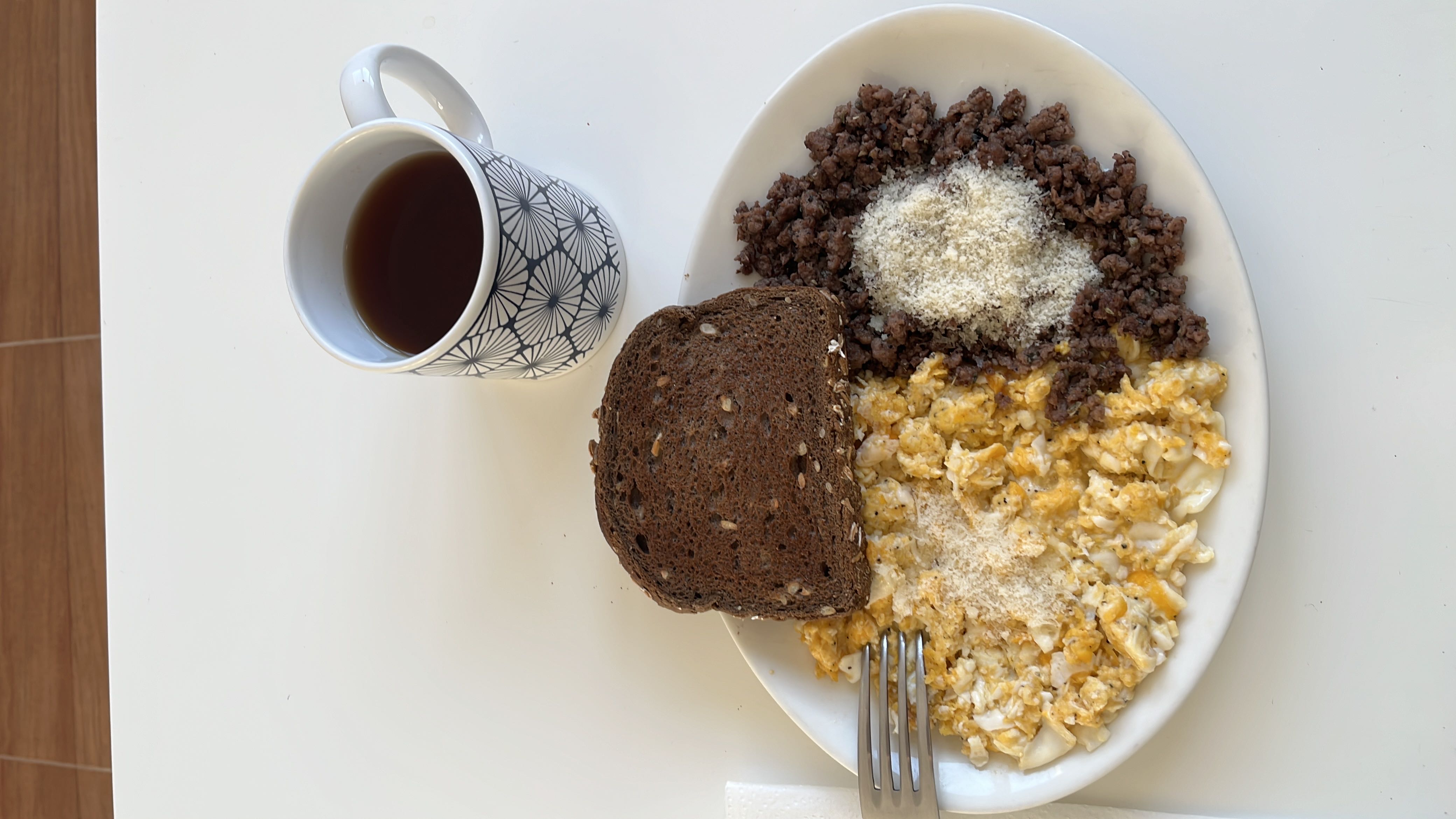 A balanced meal consisting of scrambled eggs, ground beef, whole grain bread, and a cup of black coffee.