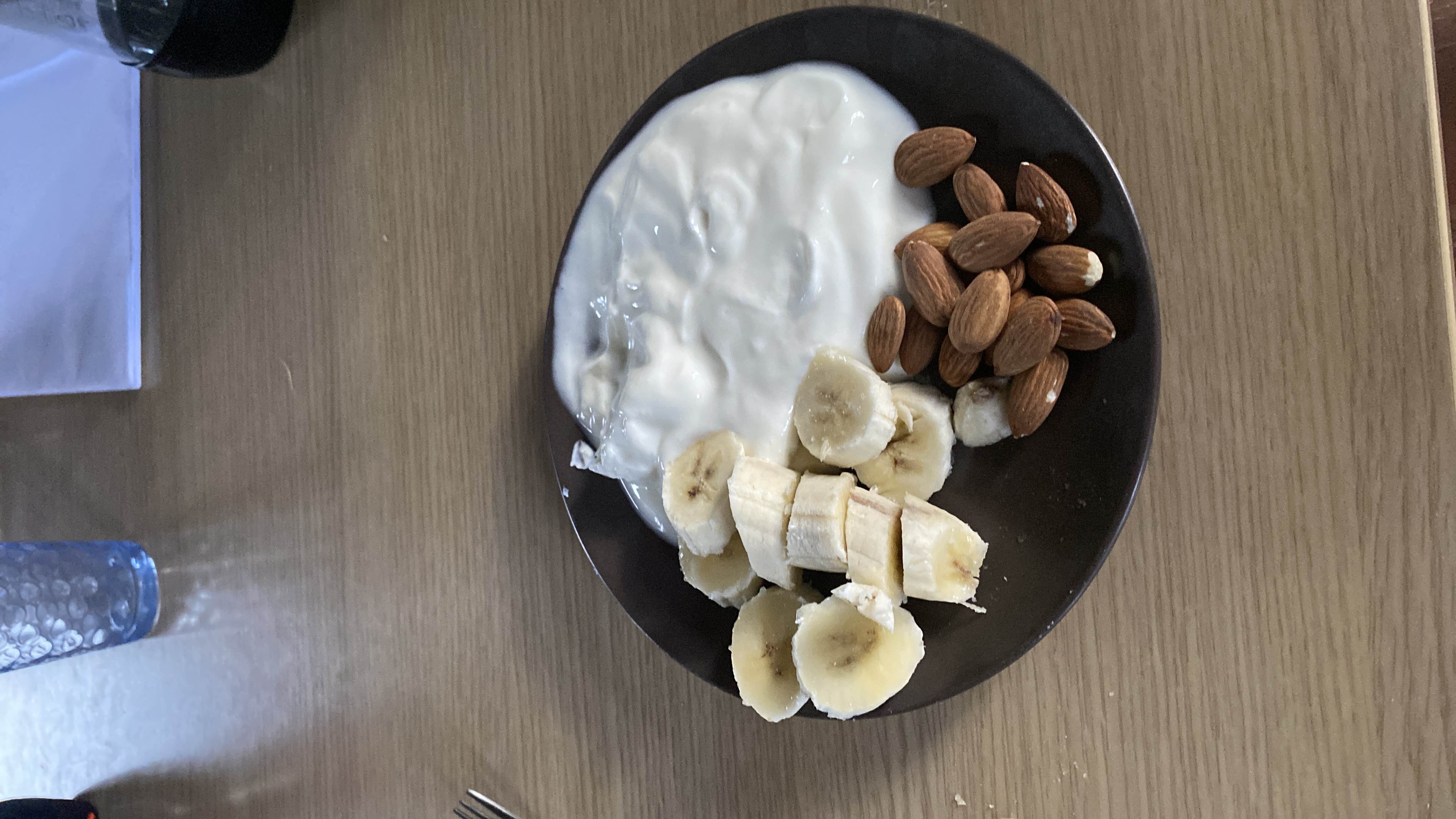 A healthy snack consisting of sliced banana, almonds, and yogurt, providing a balanced mix of protein, carbs, and fats.