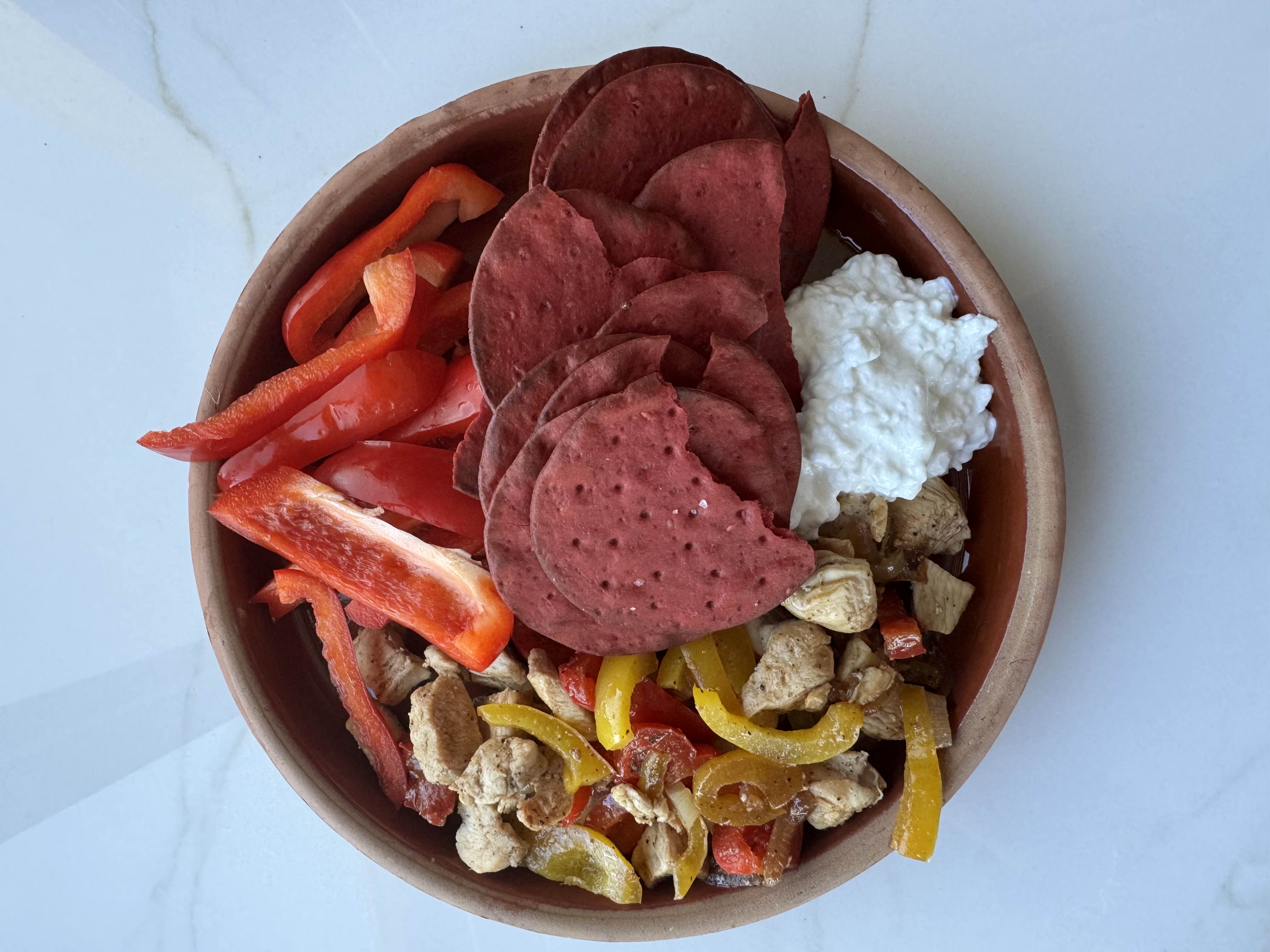 A balanced meal consisting of chicken, bell peppers, beet chips, and cottage cheese, providing a good mix of protein, carbs, and fats.