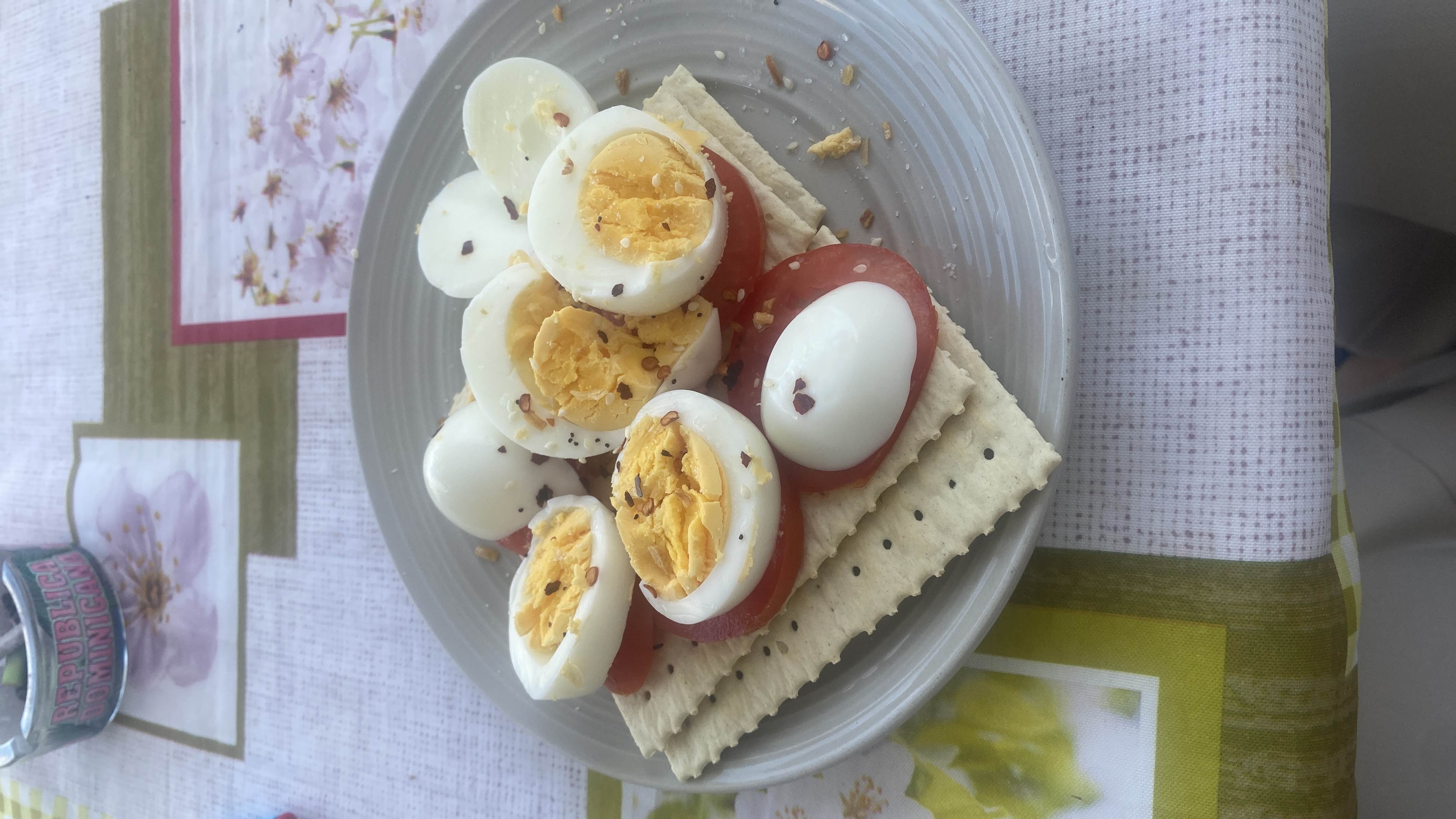 A plate of boiled eggs, tomato slices, and crackers, garnished with spices, providing a balanced mix of protein, carbs, and fats.