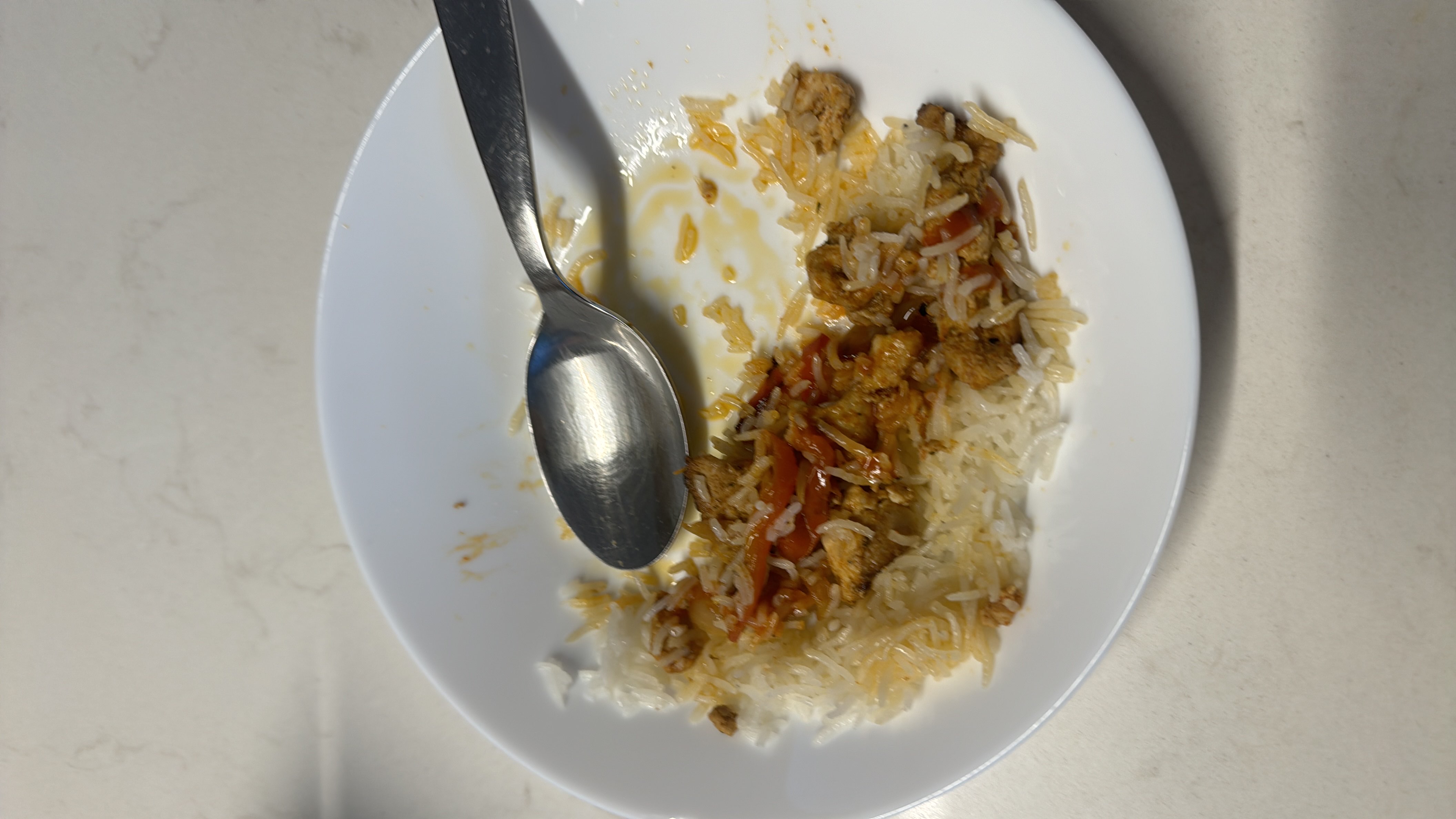 A partially eaten plate of rice, chicken, and sauce, providing a balanced mix of protein, carbs, and fats.