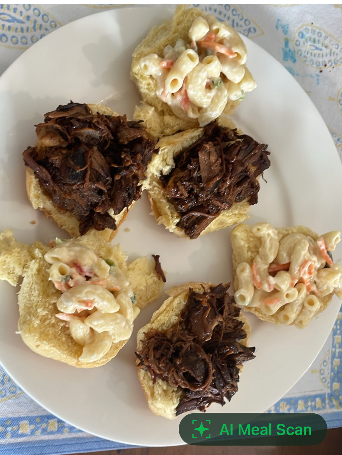 The dish consists of bread rolls topped with pulled beef and macaroni salad, providing a balanced mix of protein, carbs, and fats.