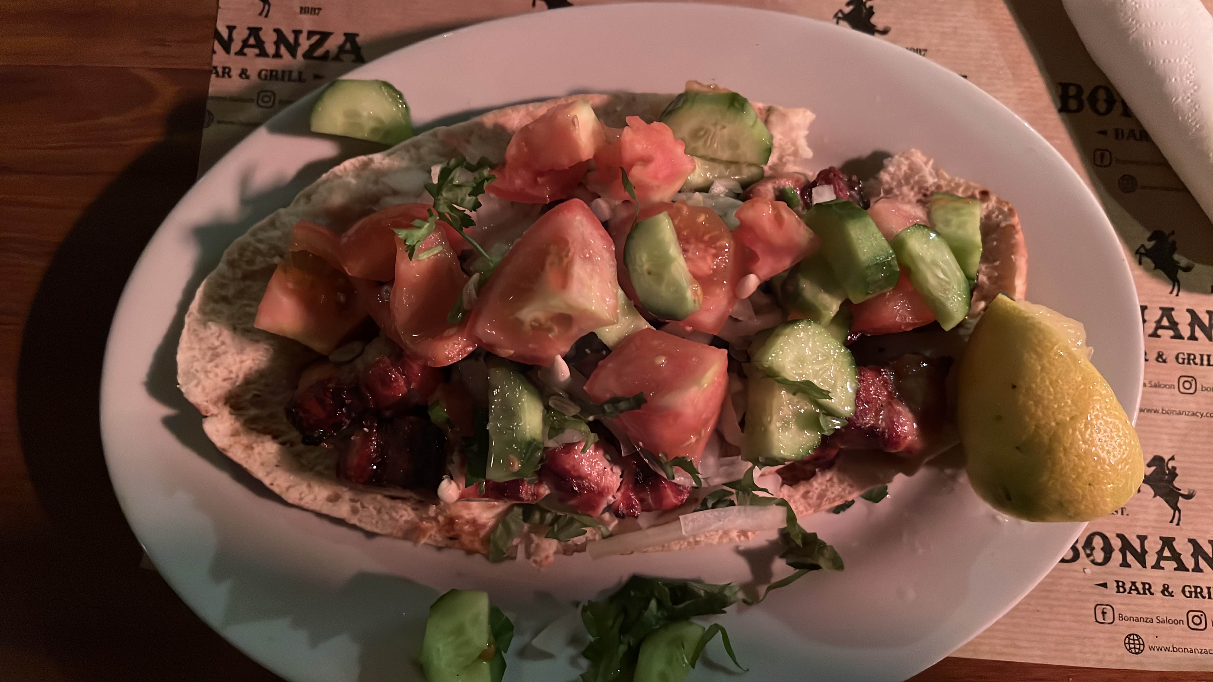 A dish consisting of pita bread topped with grilled meat, fresh cucumber, tomato, and a lemon wedge, offering a balanced mix of protein, carbs, and fats.