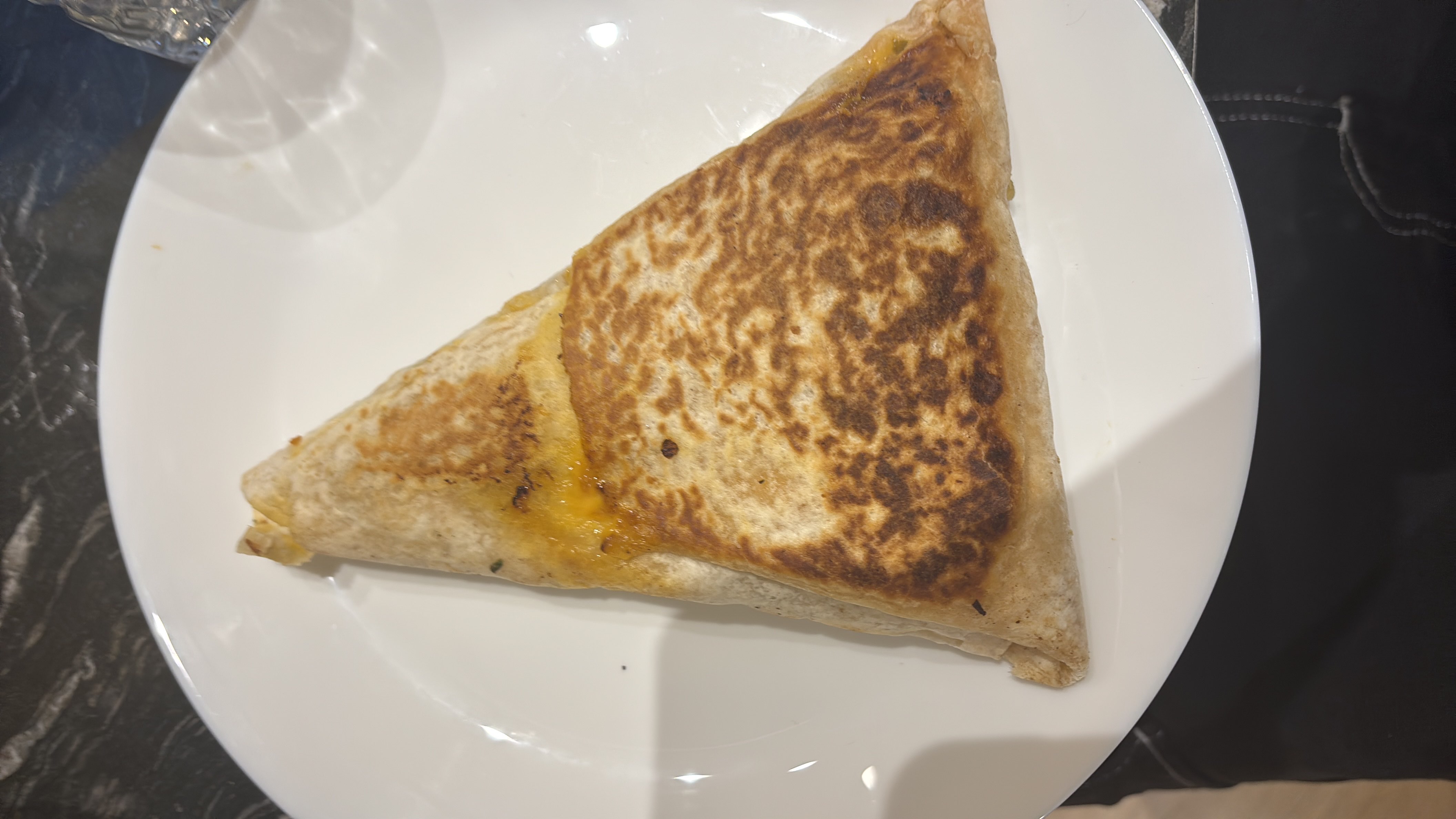 A grilled tortilla wrap filled with cheese, vegetables, and sauce, providing a balanced mix of carbs, protein, and fats.