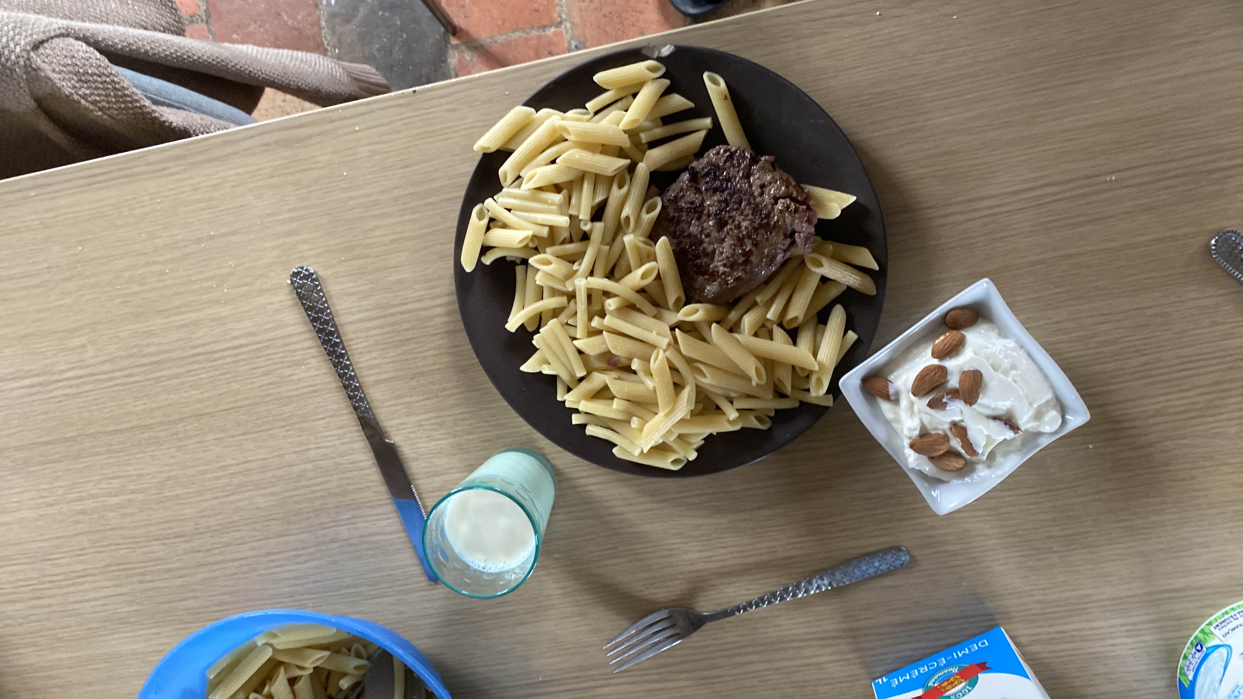 A meal consisting of pasta, a beef patty, and yogurt topped with almonds, accompanied by a glass of milk.