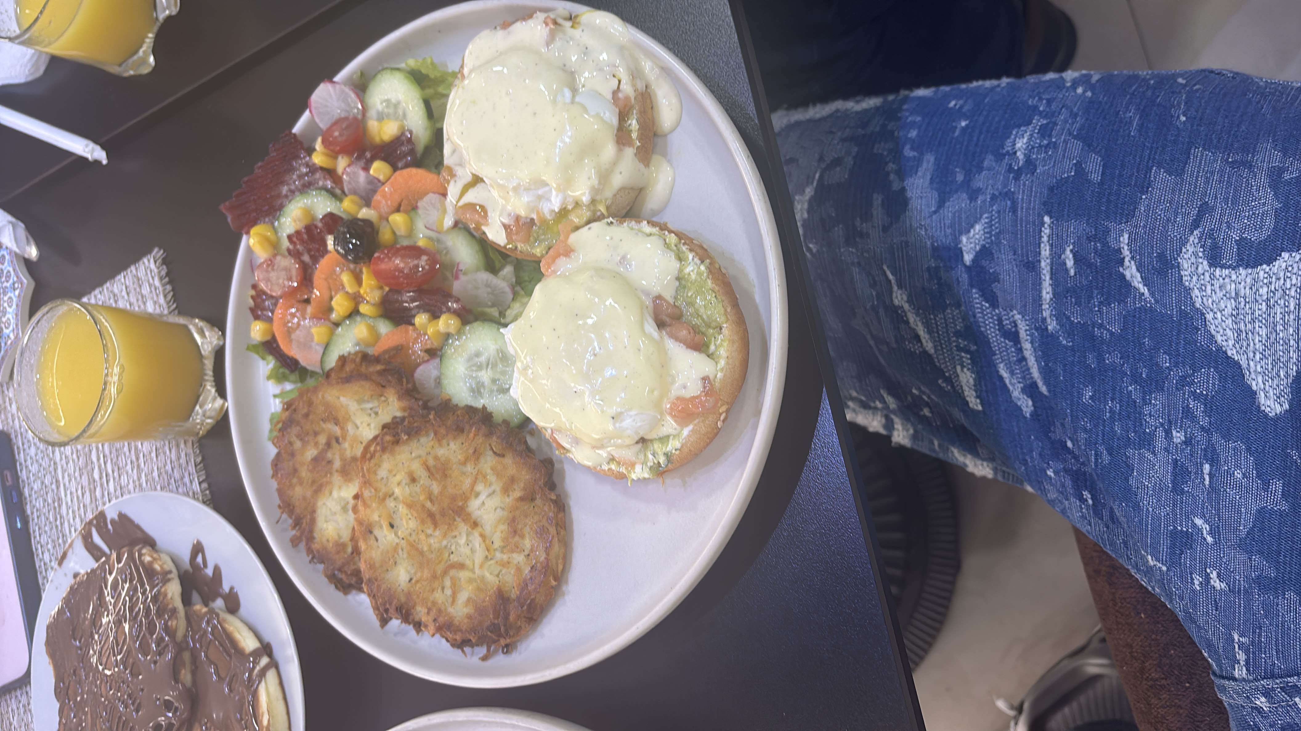 A balanced breakfast plate featuring eggs benedict, hash browns, a fresh salad, pancakes with chocolate, and orange juice.