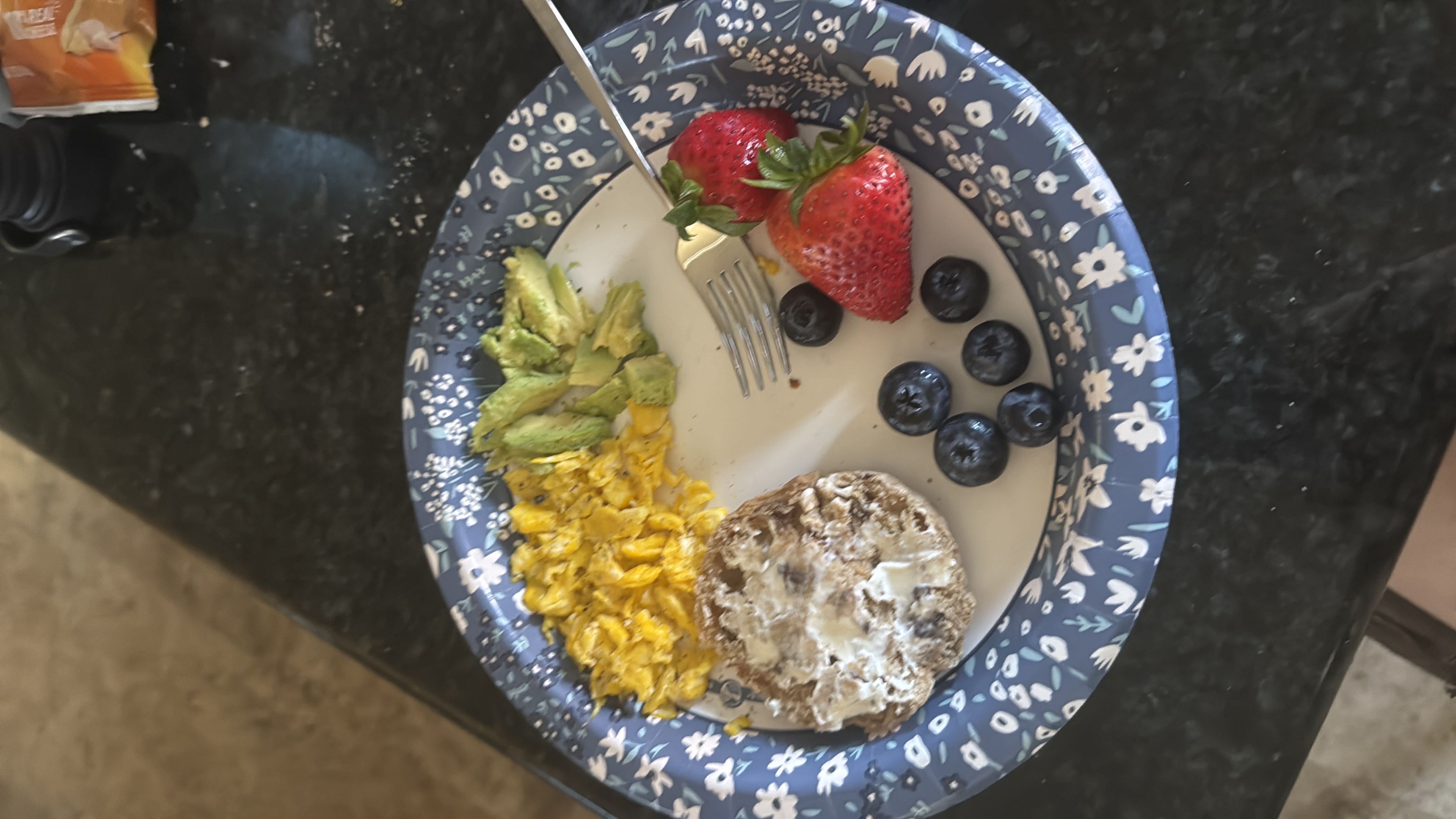 A breakfast including a brown egg, almost half an avocado, a 75-calorie cinnamon raisin English muffin half, reduced fat cream cheese, two strawberries, and six blueberries.