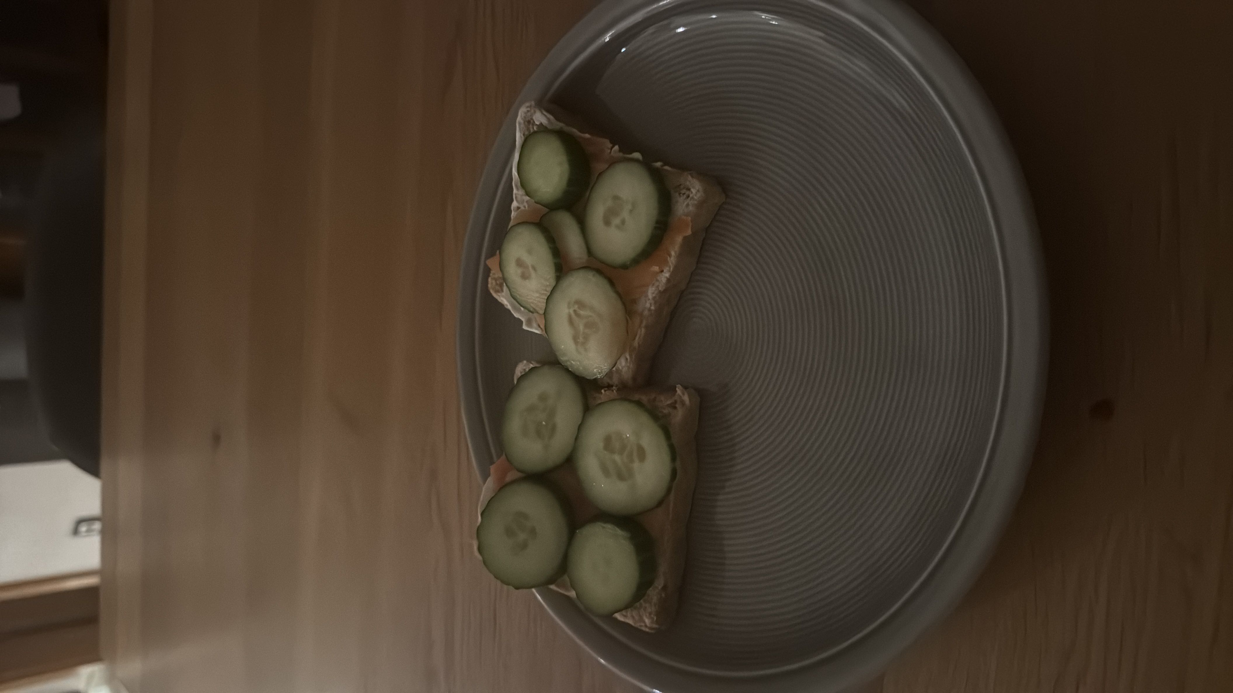 A light snack consisting of bread topped with cream cheese, cucumber slices, and salmon, offering a balanced mix of carbs, fats, and protein.