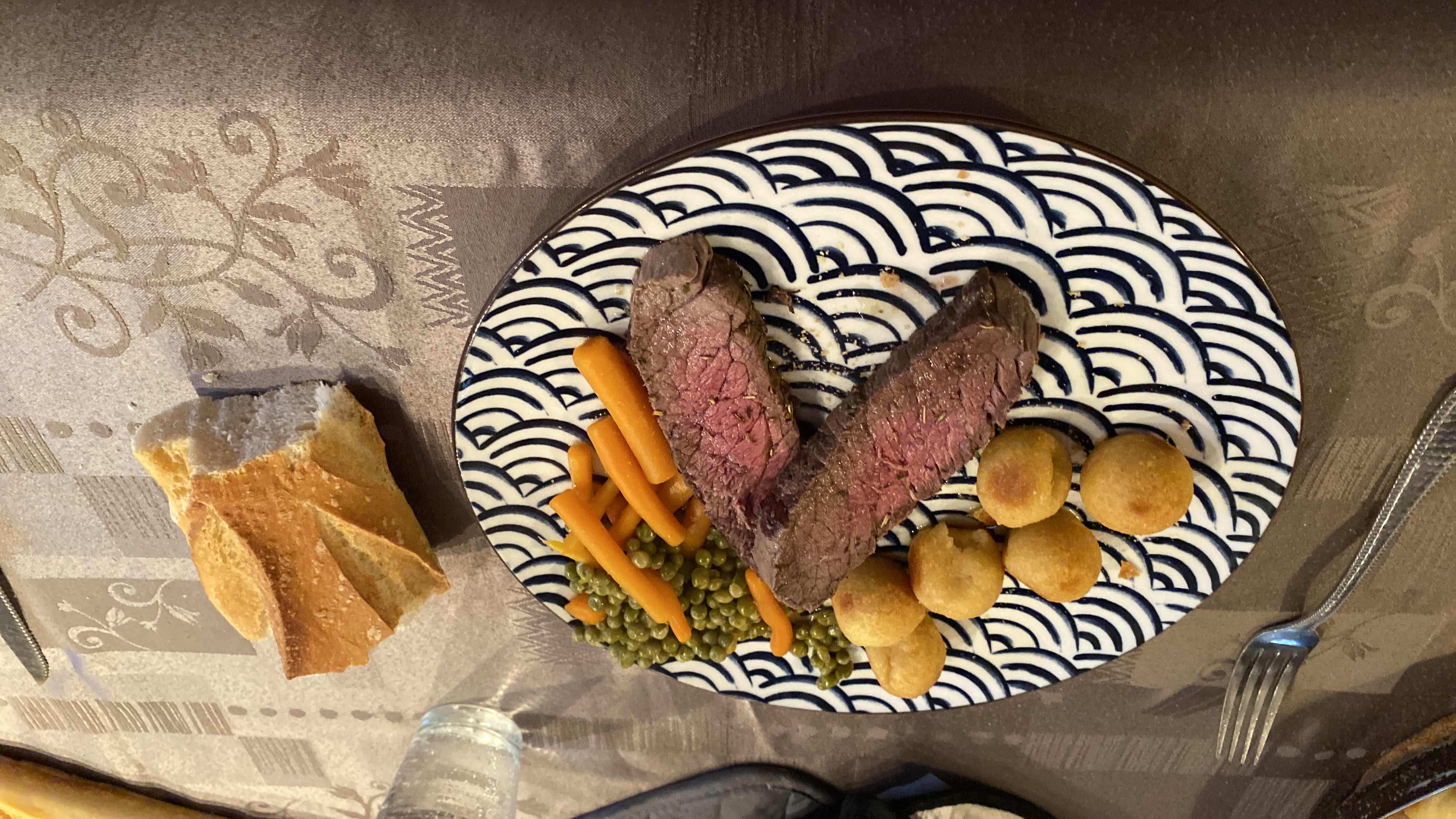 A balanced meal consisting of beef steak, peas, carrots, potato croquettes, and bread.