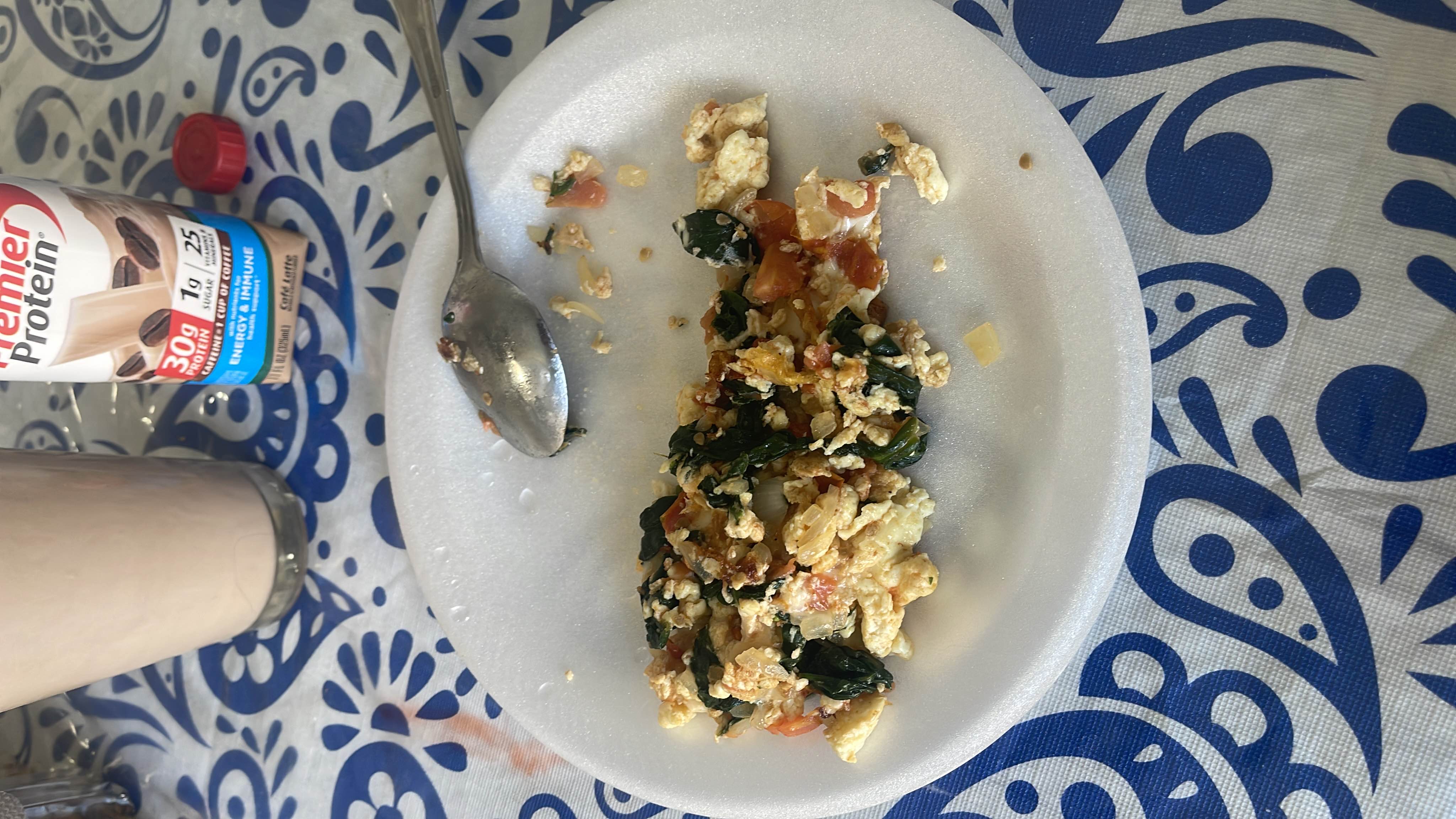A high-protein meal consisting of scrambled eggs with spinach and tomatoes, accompanied by a Premier Protein shake.