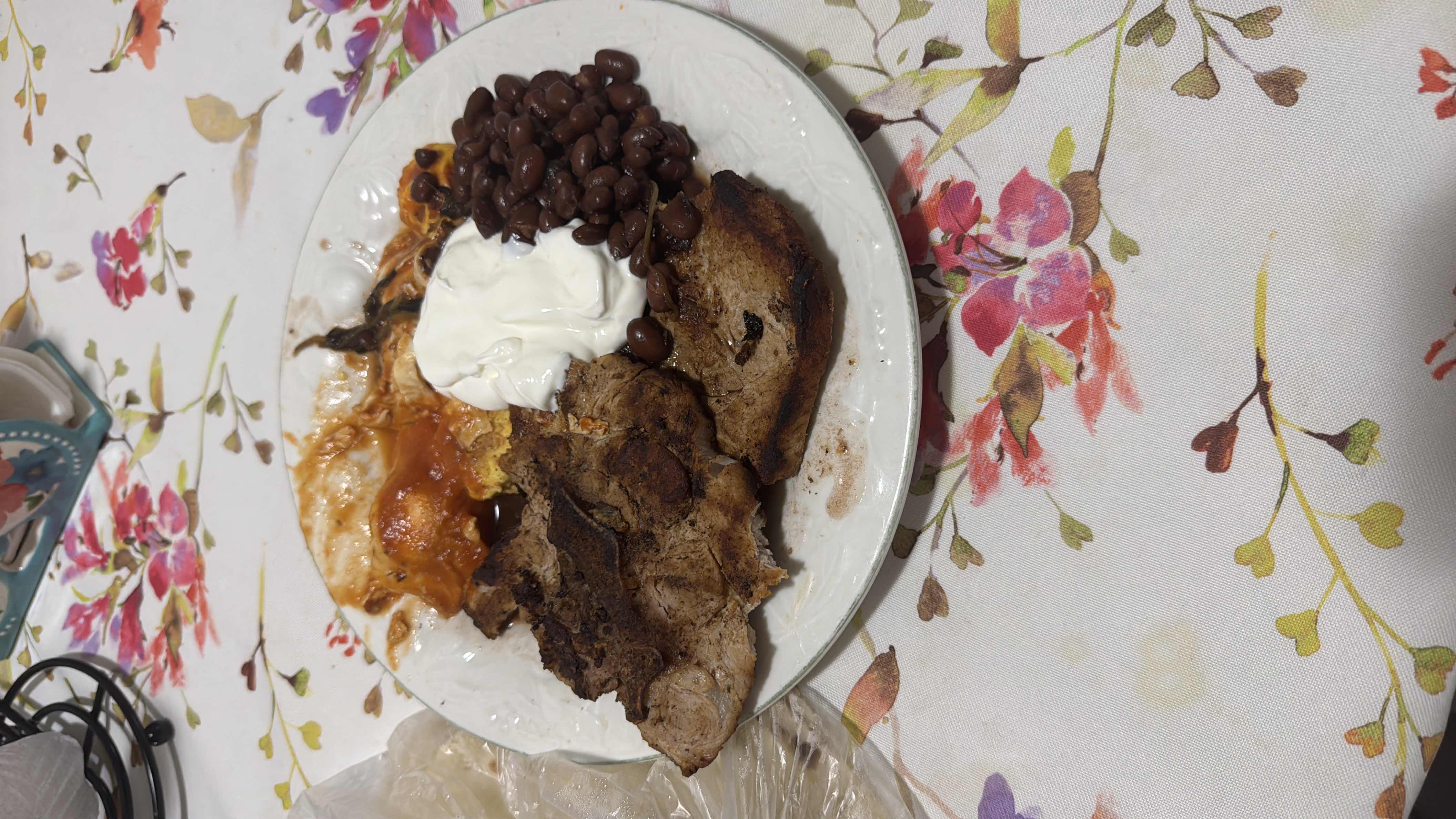 A plate containing grilled meat, beans, sour cream, tomato sauce, and cornbread, providing a balanced mix of protein, carbs, and fats.