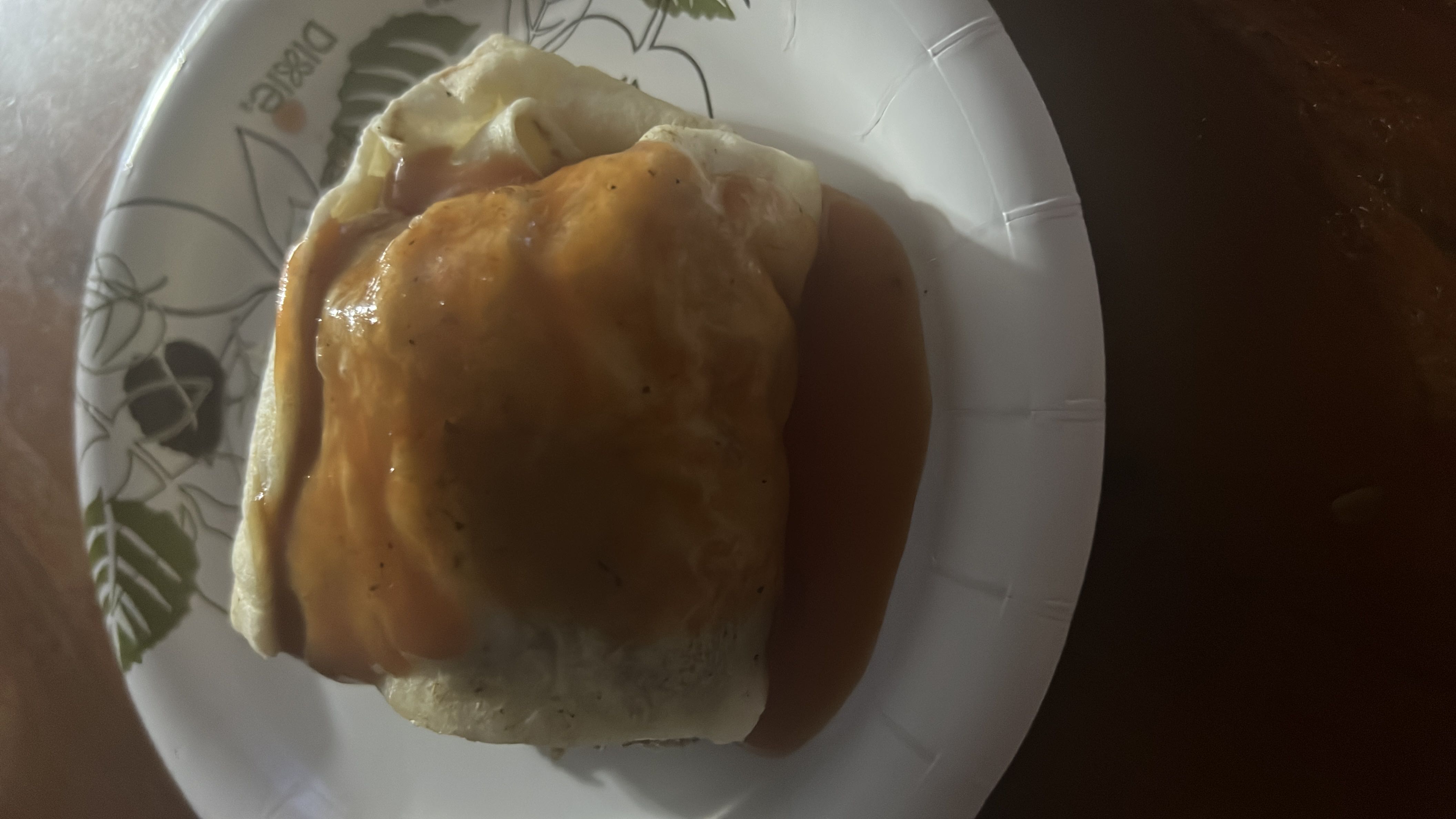 A wrapped tortilla dish topped with a savory sauce, containing cheese and a filling.