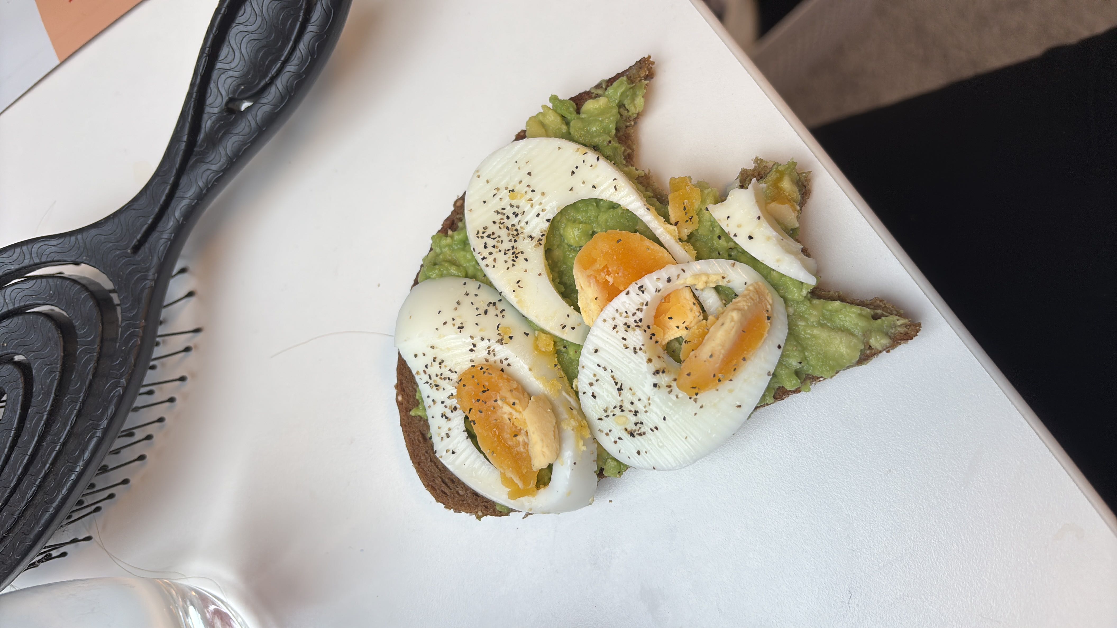 A slice of whole grain bread topped with mashed avocado, boiled egg slices, and a sprinkle of black pepper.