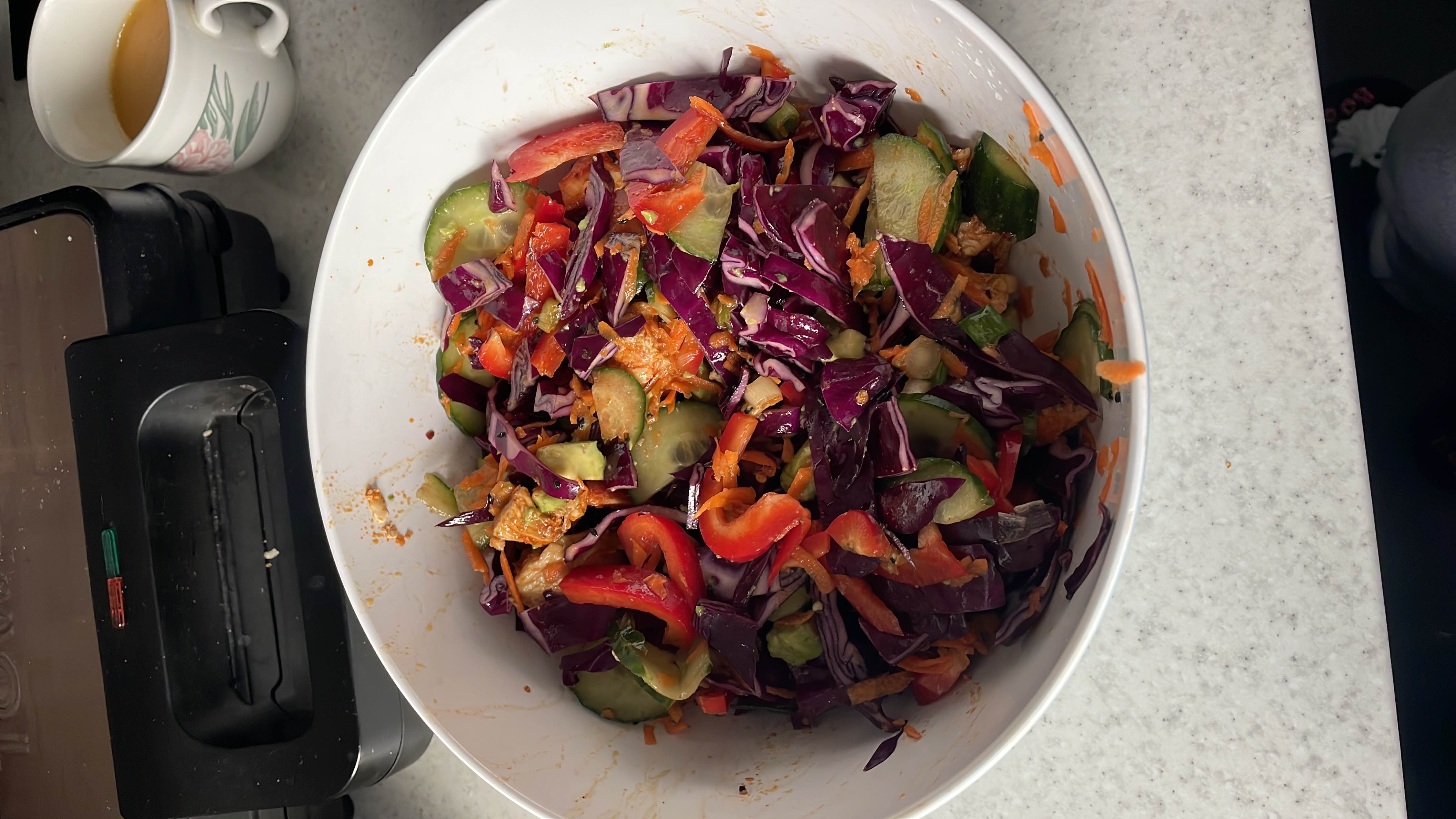 A colorful vegetable salad with red cabbage, cucumber, red bell pepper, carrot, avocado, chicken, soy sauce, and sesame oil, providing a healthy mix of nutrients.