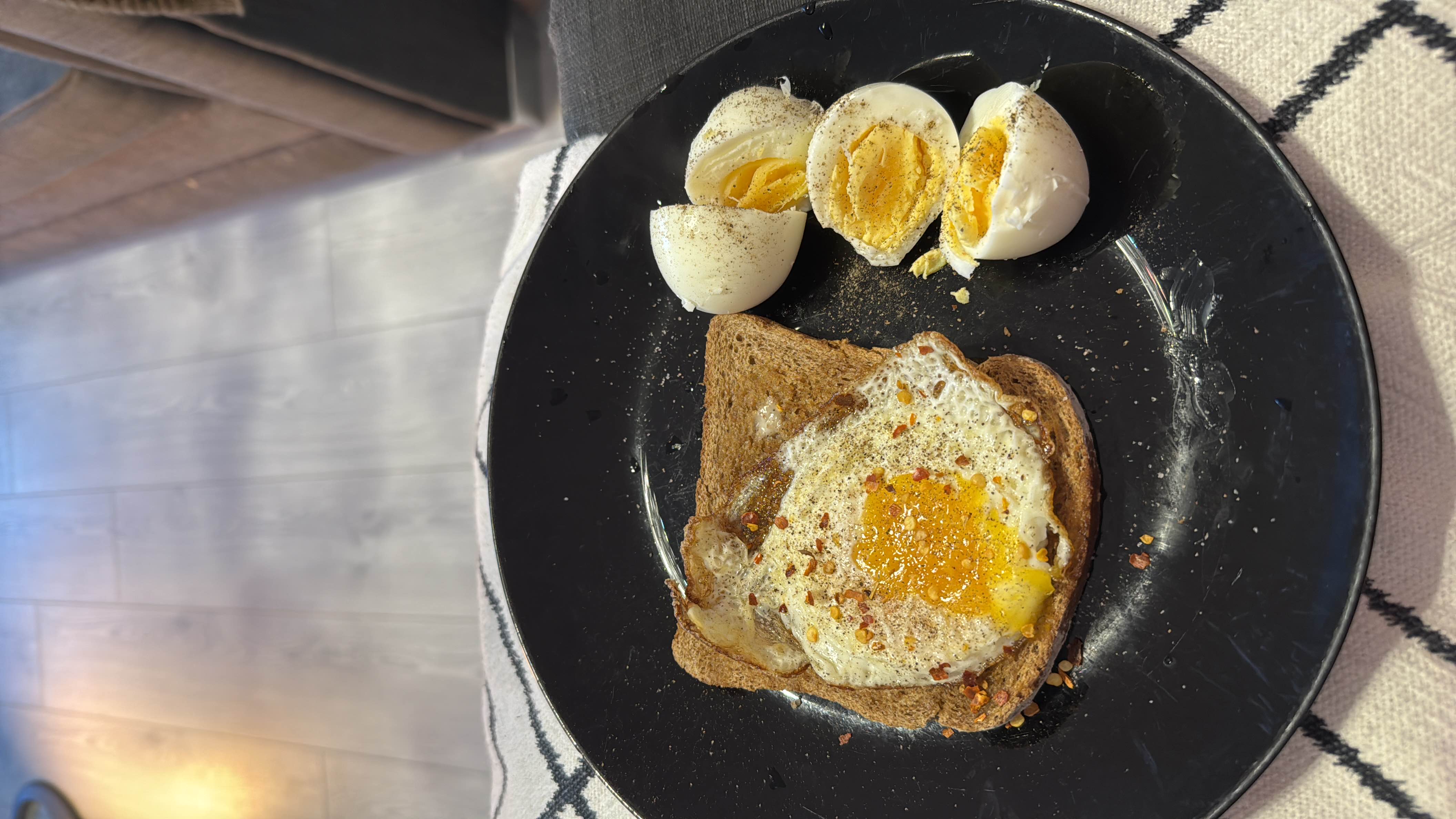A nutritious meal consisting of a slice of whole grain bread with a fried egg and a boiled egg, seasoned with spices.
