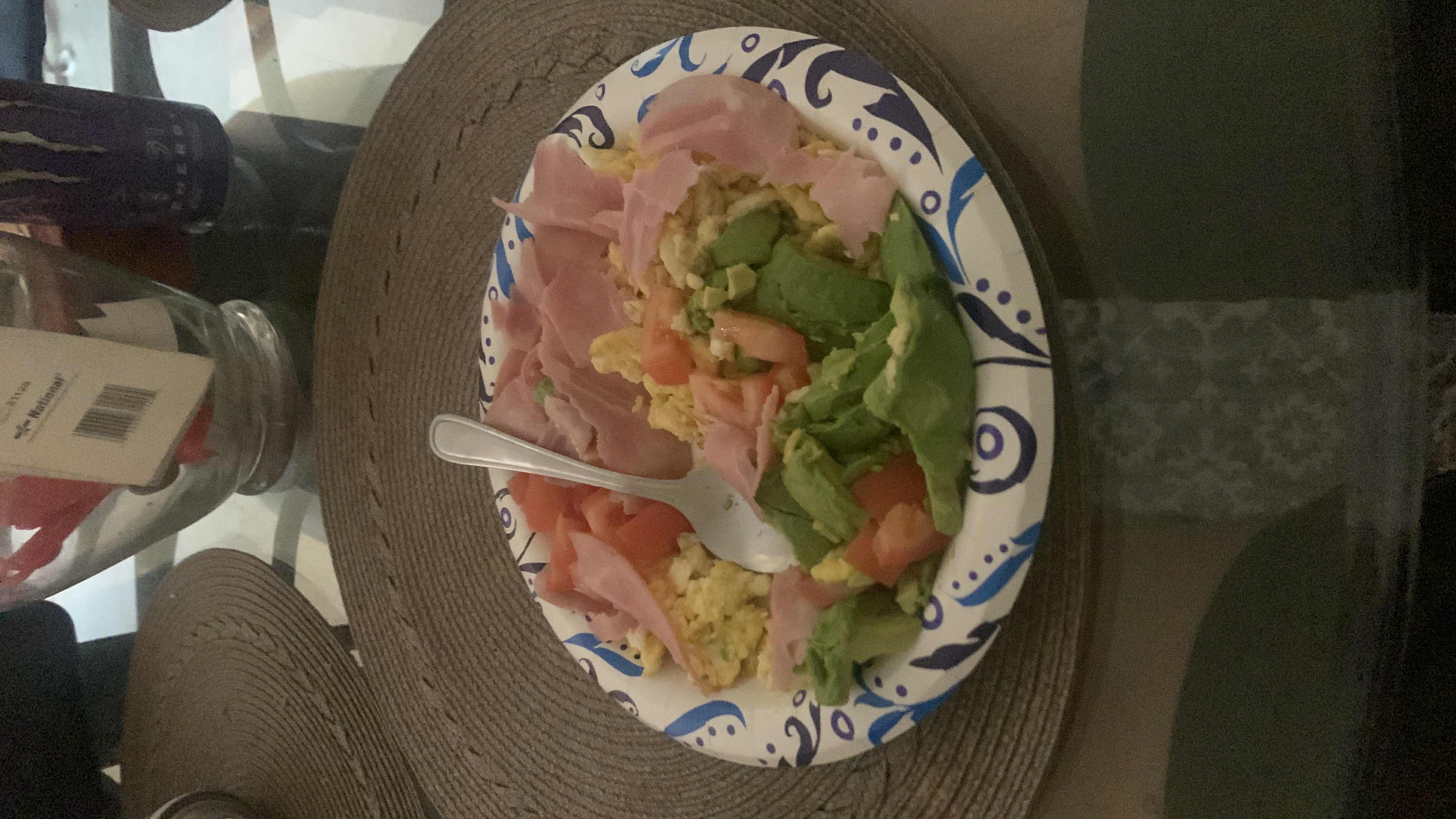 A plate containing scrambled eggs, ham, avocado, and tomato, providing a balanced mix of protein, healthy fats, and minimal carbs.