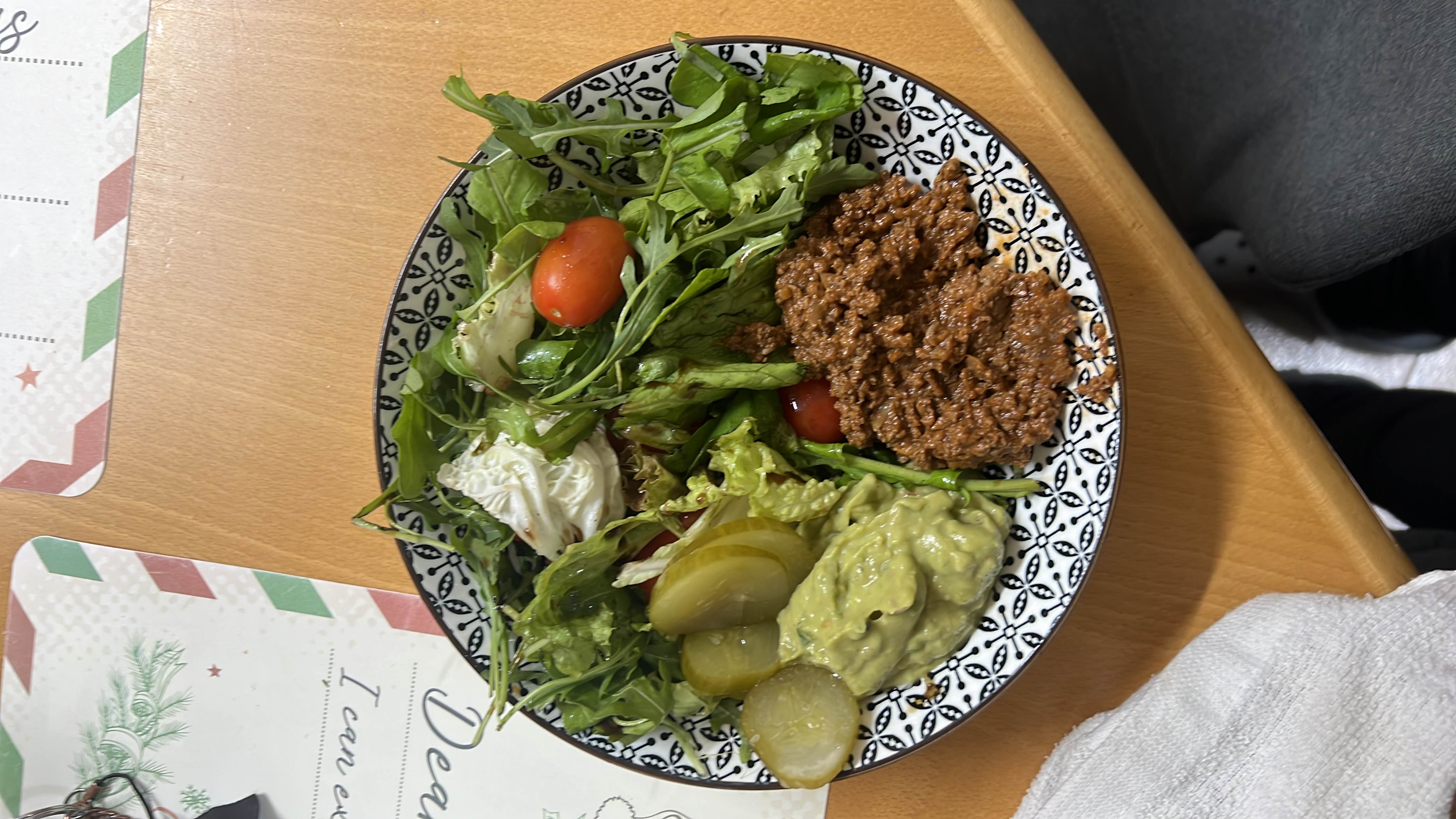 A healthy plate consisting of ground beef, mixed greens, cherry tomatoes, pickles, and guacamole.