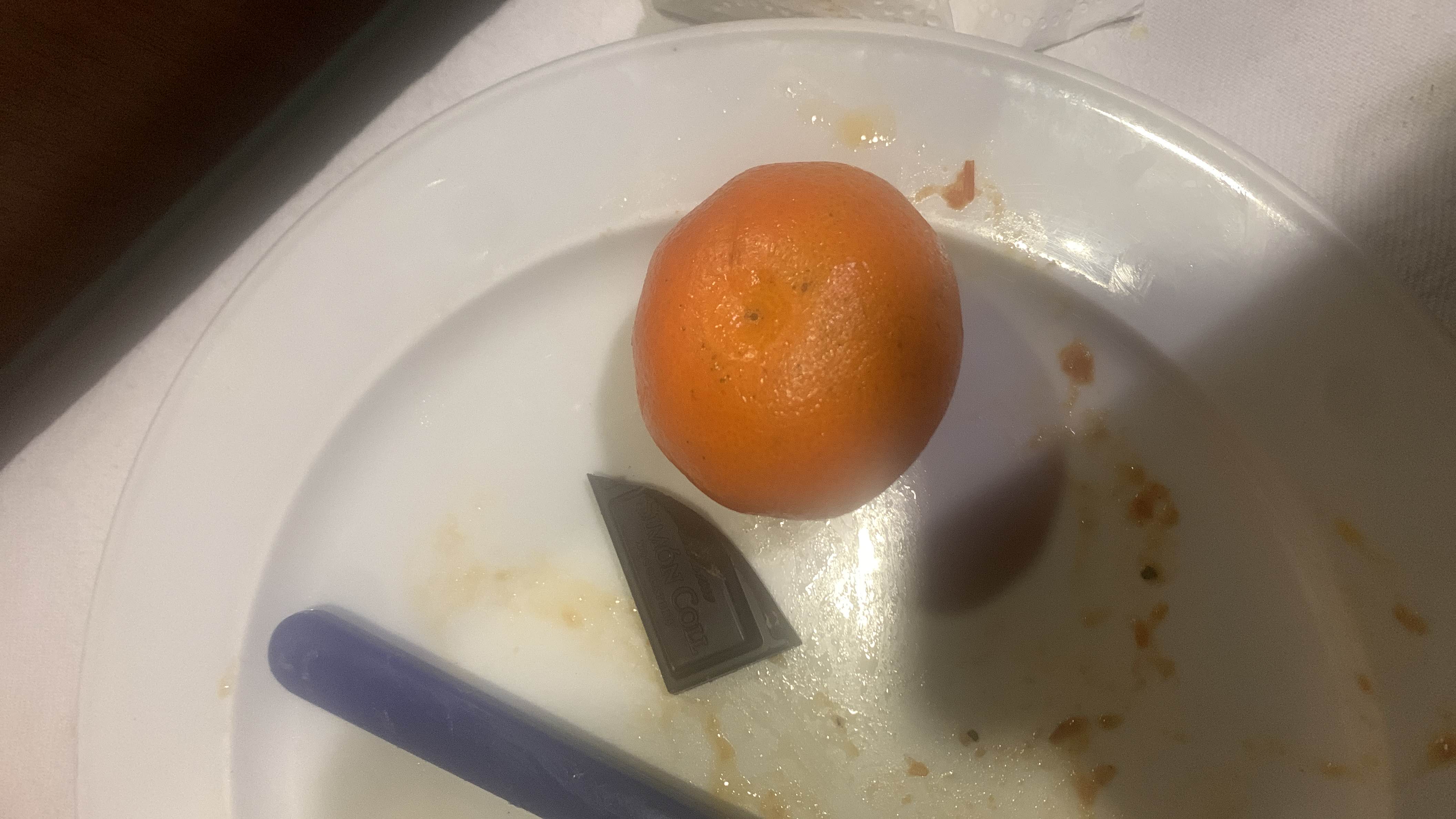A plate containing a mandarin orange and a piece of dark chocolate, providing a light and nutritious snack.