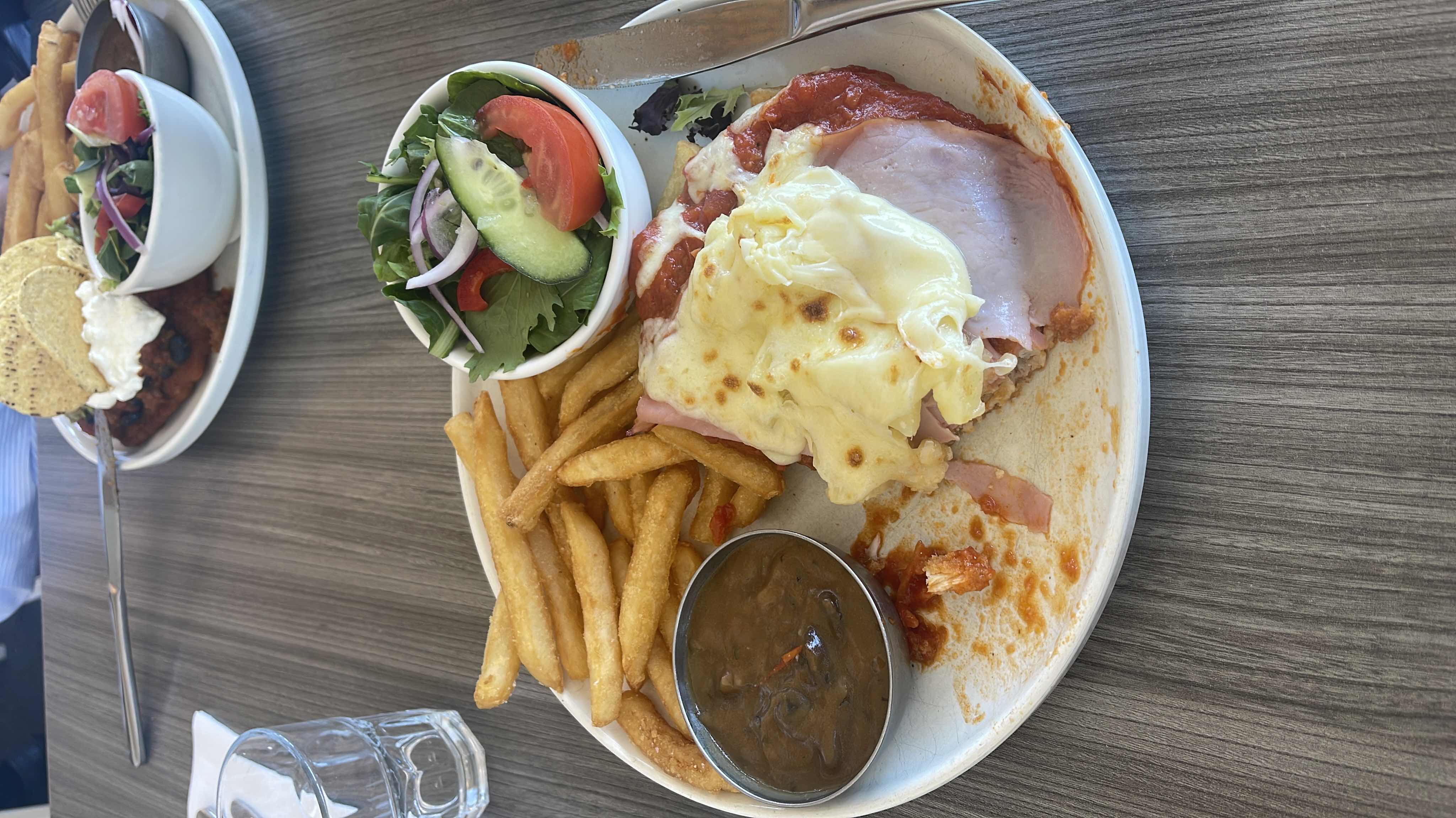 A plate containing ham topped with melted cheese, fries, a side salad, and a small bowl of gravy.
