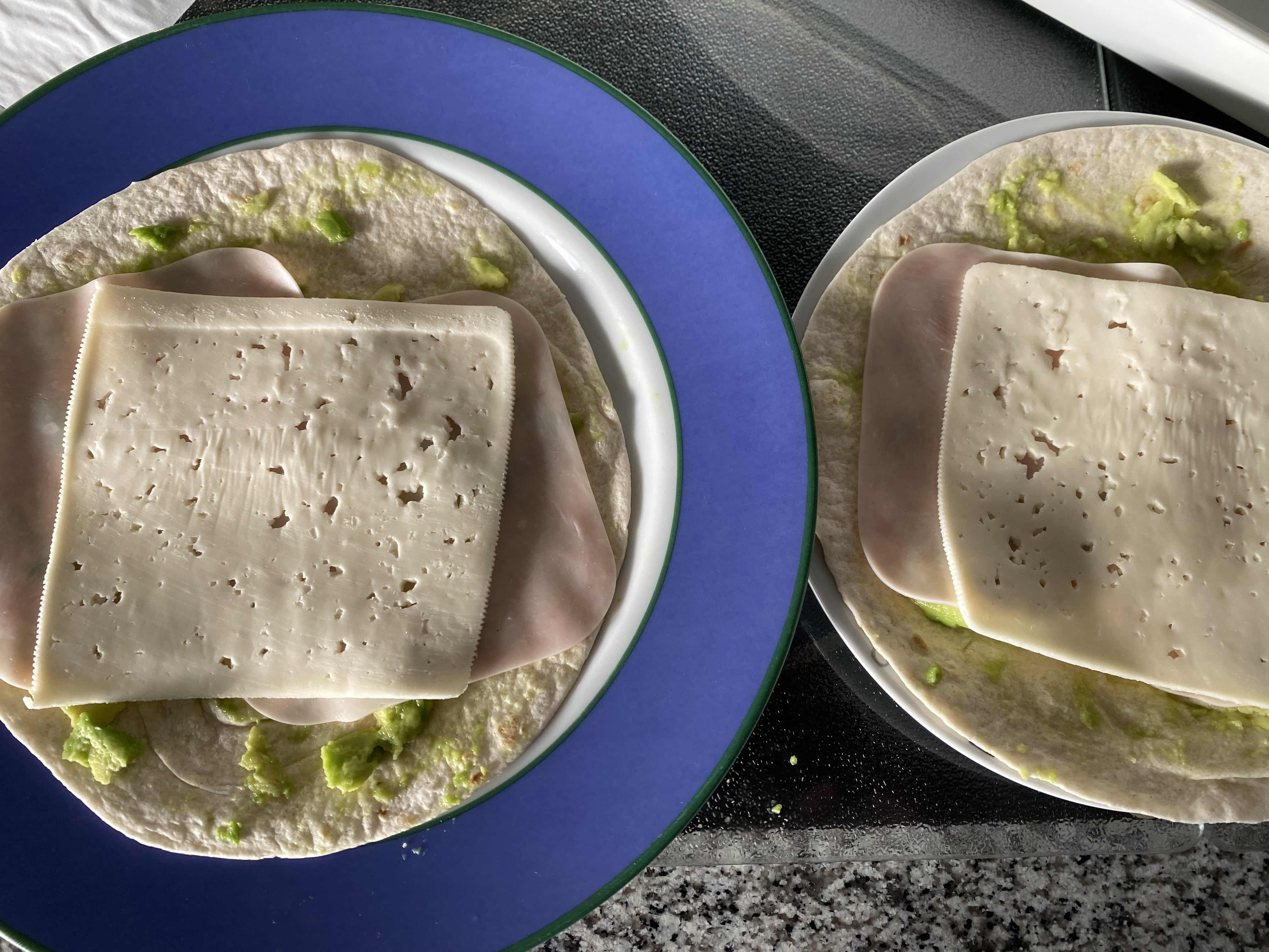A simple wrap made with tortilla, cheese, turkey slices, and avocado spread.