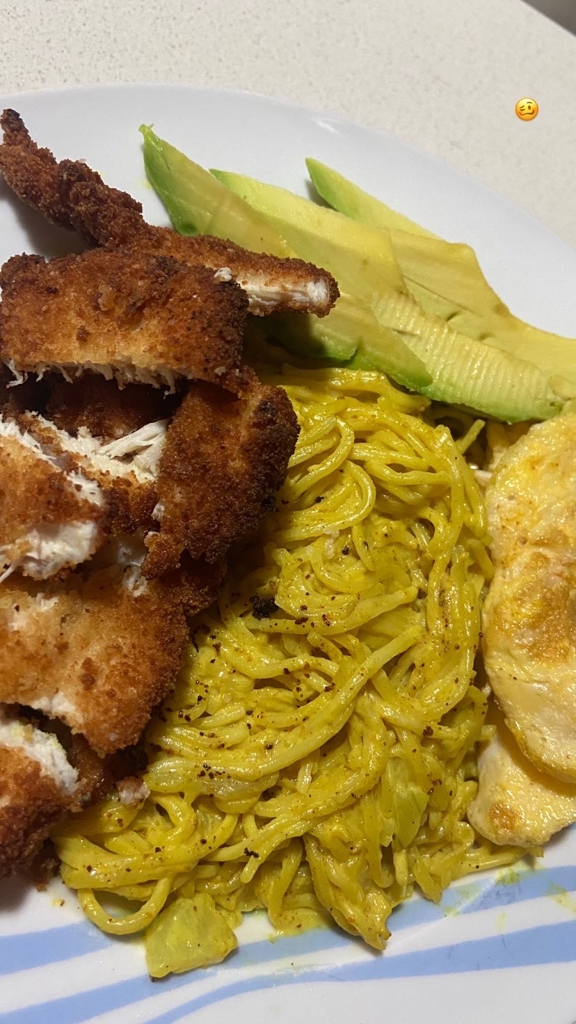 A dish consisting of breaded chicken, creamy pasta, and sliced avocado, providing a balanced mix of protein, carbs, and fats.