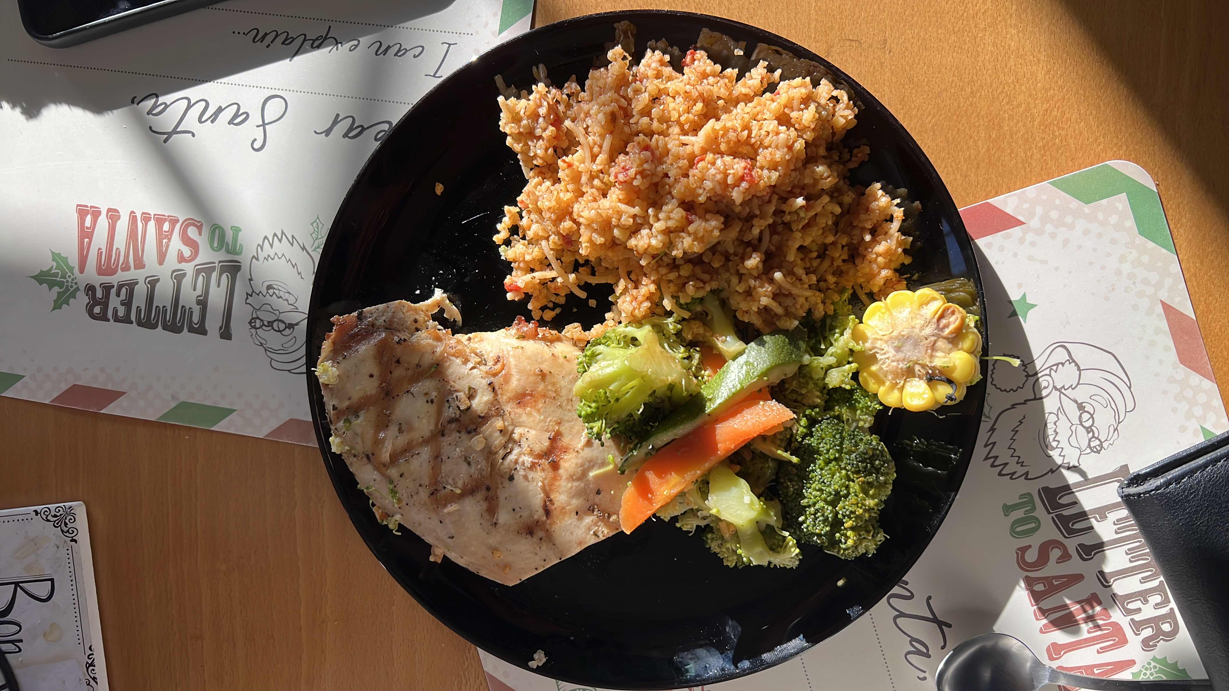 A balanced meal consisting of grilled chicken, mixed vegetables, rice pilaf, and a piece of corn, providing a good mix of protein, carbs, and fats.