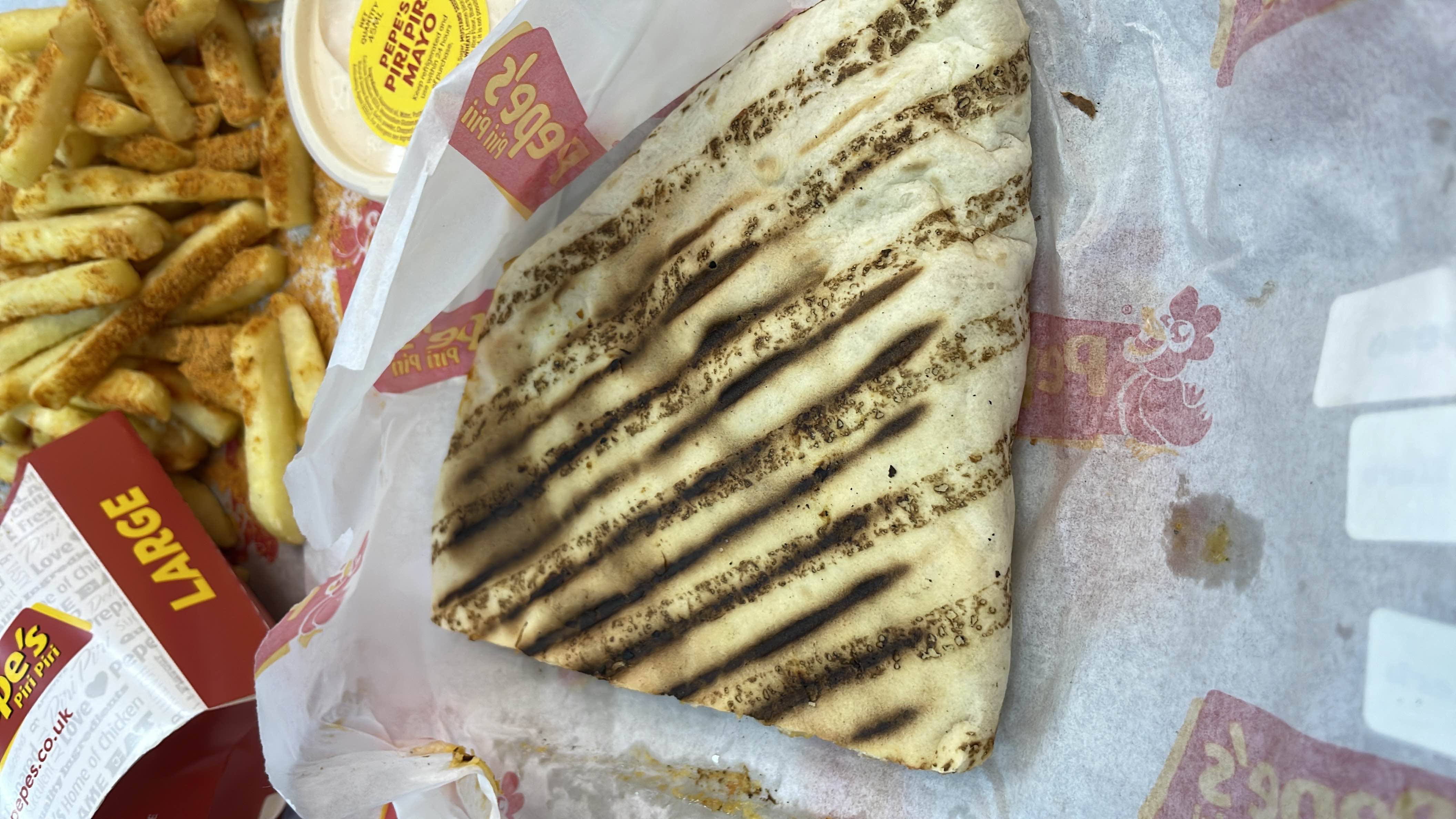 A grilled wrap served with seasoned fries and a side of Piri Piri mayo.