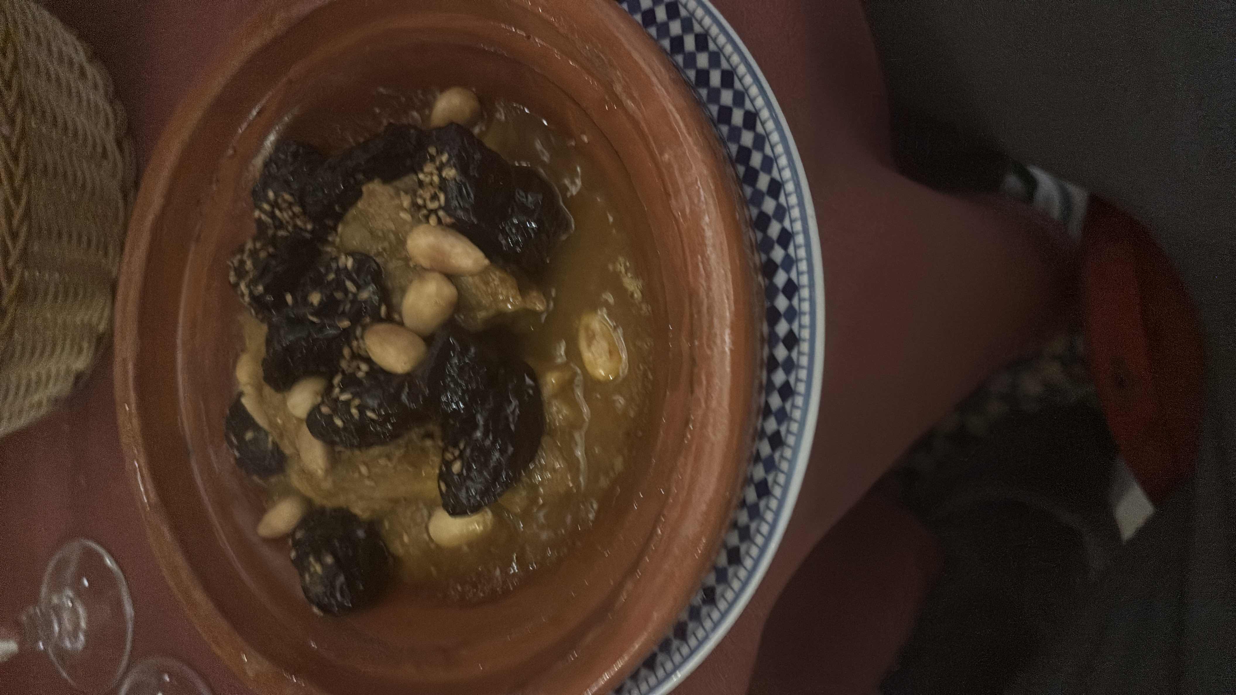 A traditional dish featuring lamb, prunes, almonds, and a savory sauce, served in a clay pot.