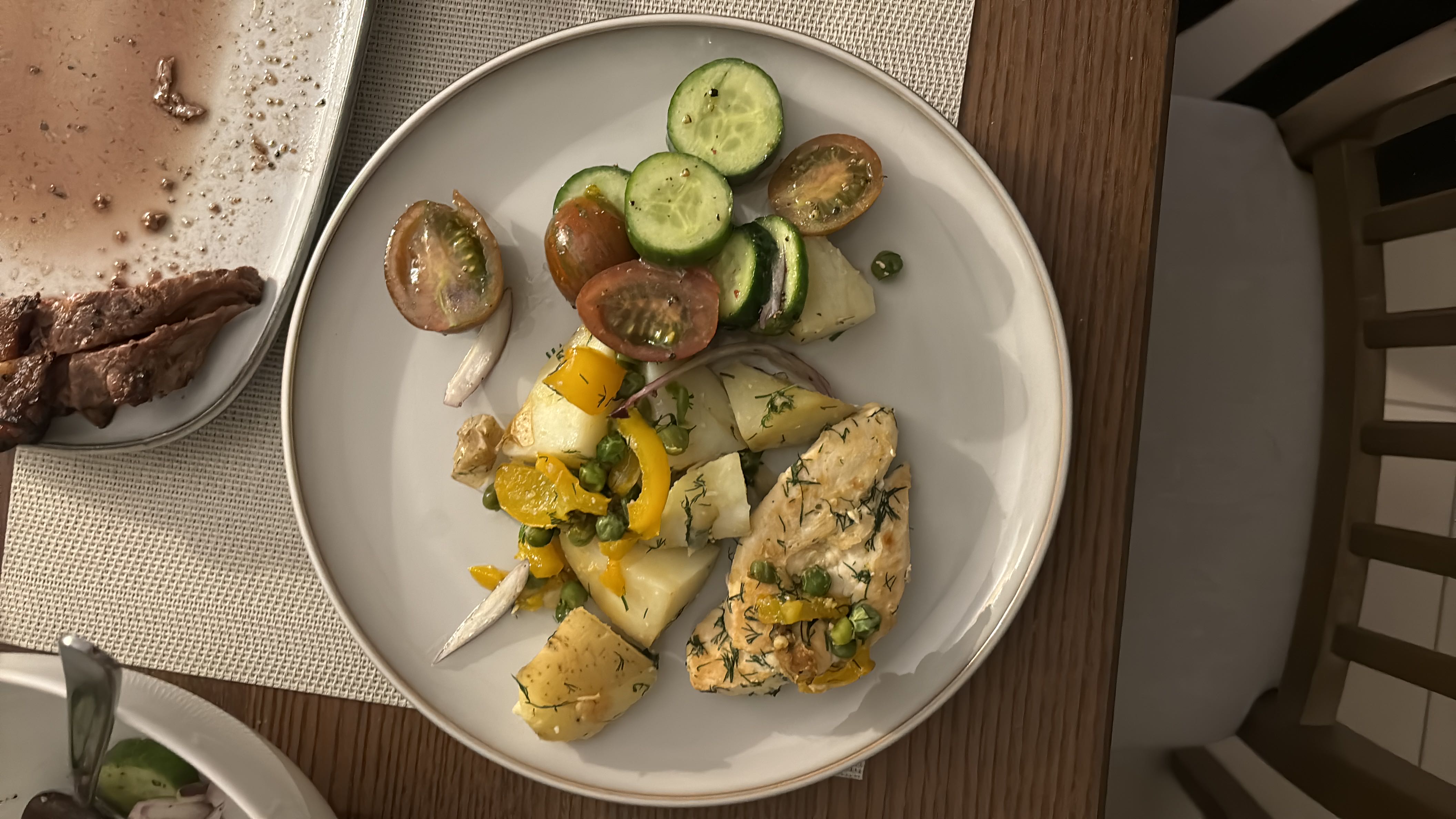 A balanced meal consisting of chicken breast, potatoes, yellow bell peppers, green peas, cucumber, and cherry tomatoes, providing a good mix of protein, carbs, and fats.