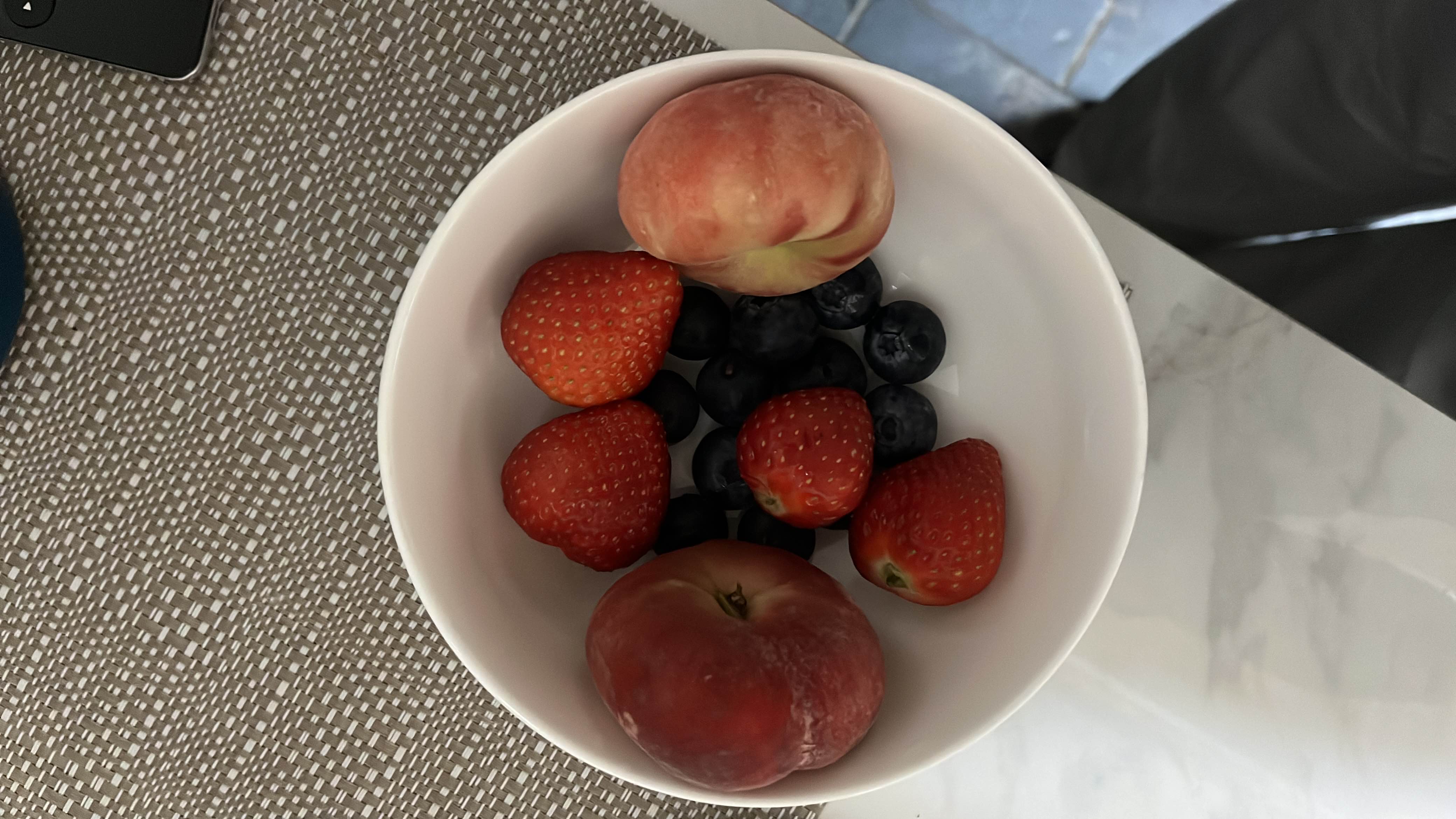 A bowl of fresh fruits including peaches, strawberries, and blueberries, providing a healthy and nutrient-rich snack.