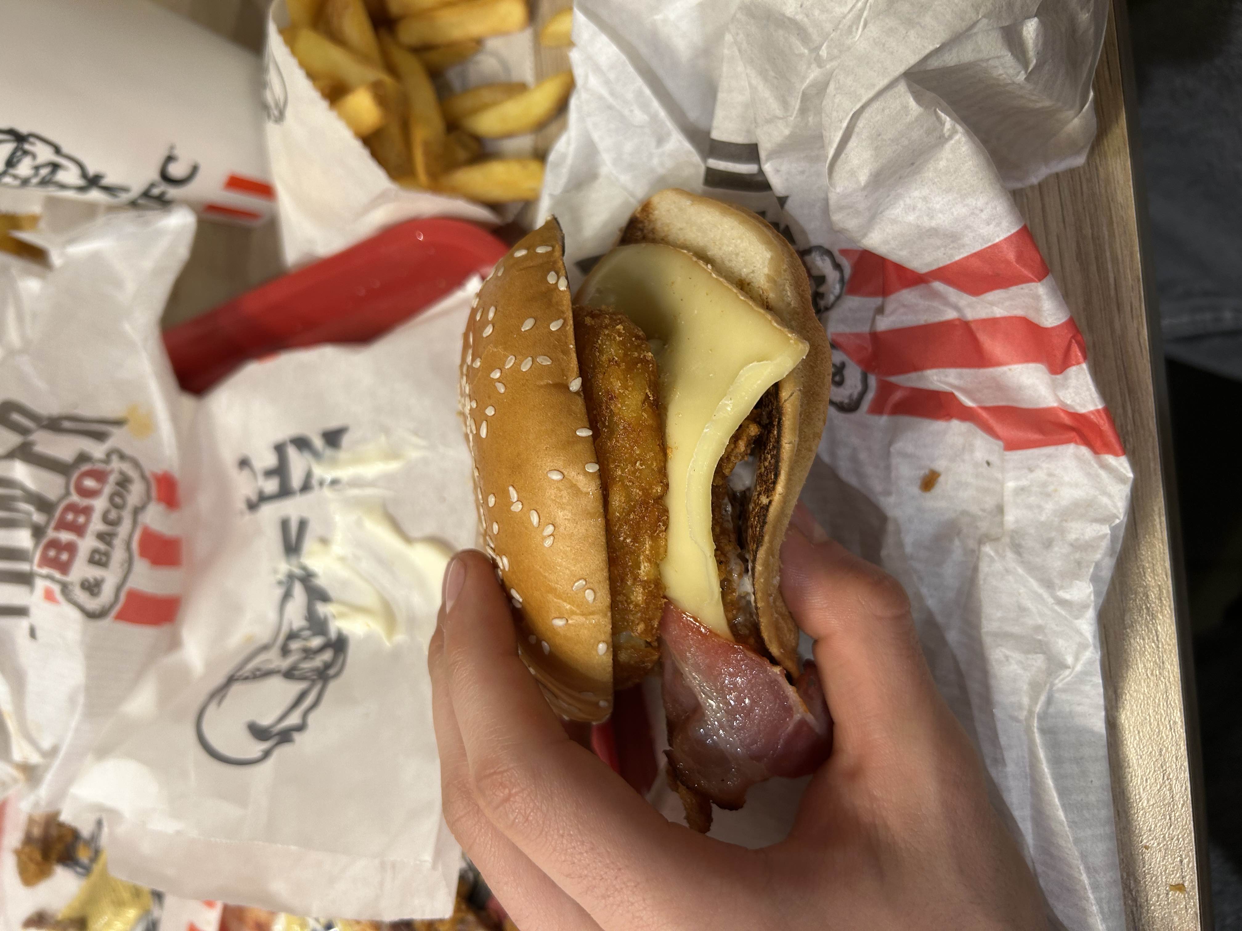 A high-calorie burger with fried chicken, bacon, cheese, onion ring, and sauce served in a sesame seed bun.