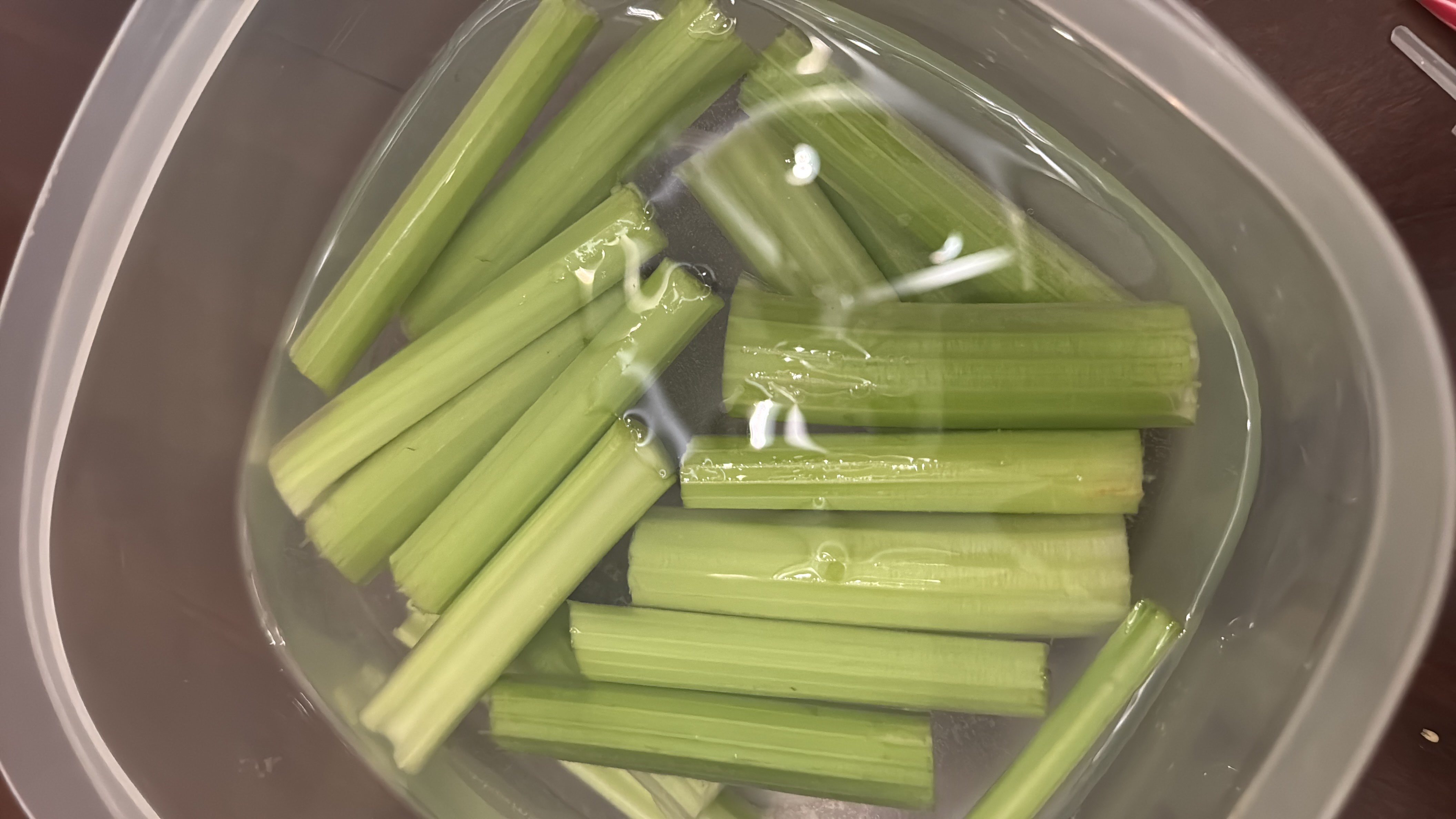 The image shows celery sticks submerged in water, a low-calorie vegetable rich in fiber and hydration.