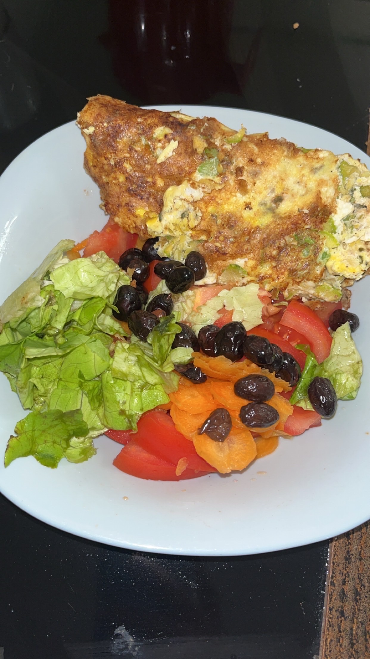 A nutritious dish featuring an egg omelette served with a fresh salad of lettuce, tomatoes, carrots, and black olives.