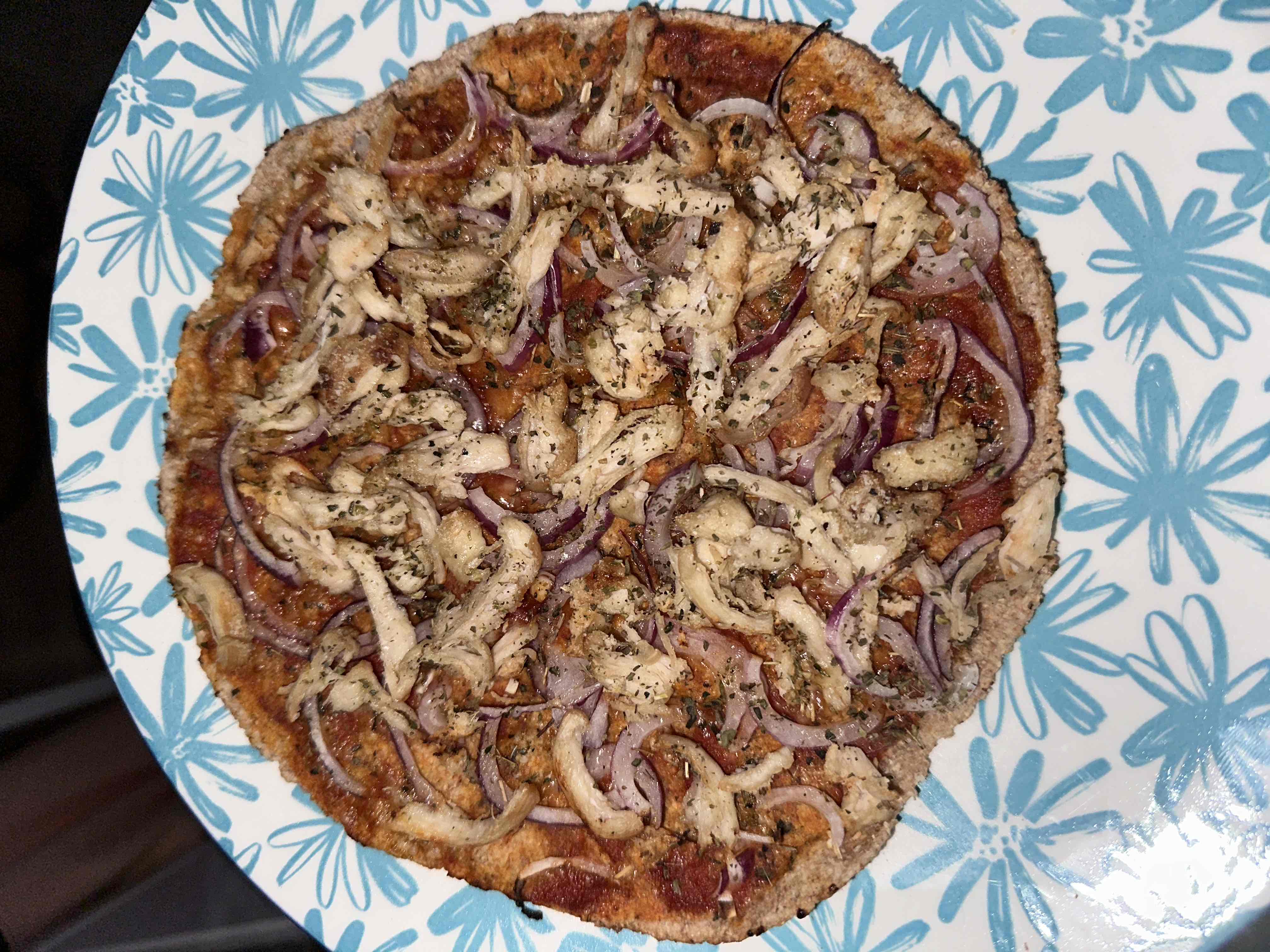 A healthy chicken pizza with a whole wheat base, topped with red onions and tomato sauce.