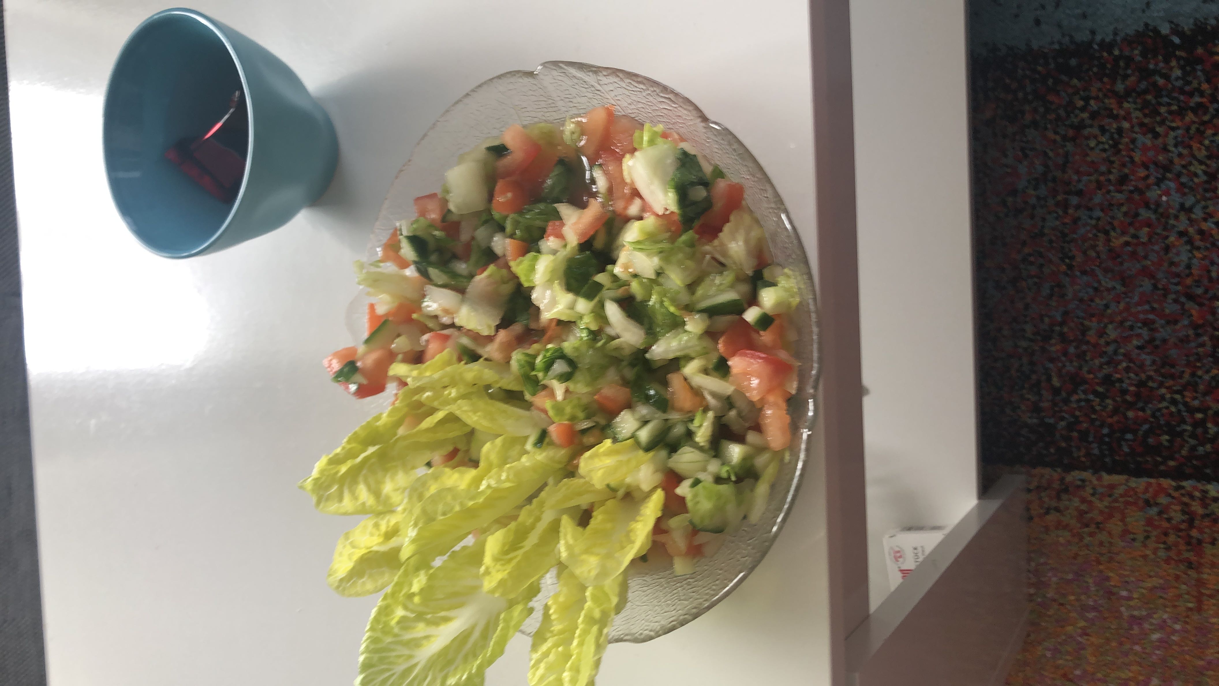 A fresh vegetable salad with lettuce, tomato, cucumber, and onion, served in a glass bowl.