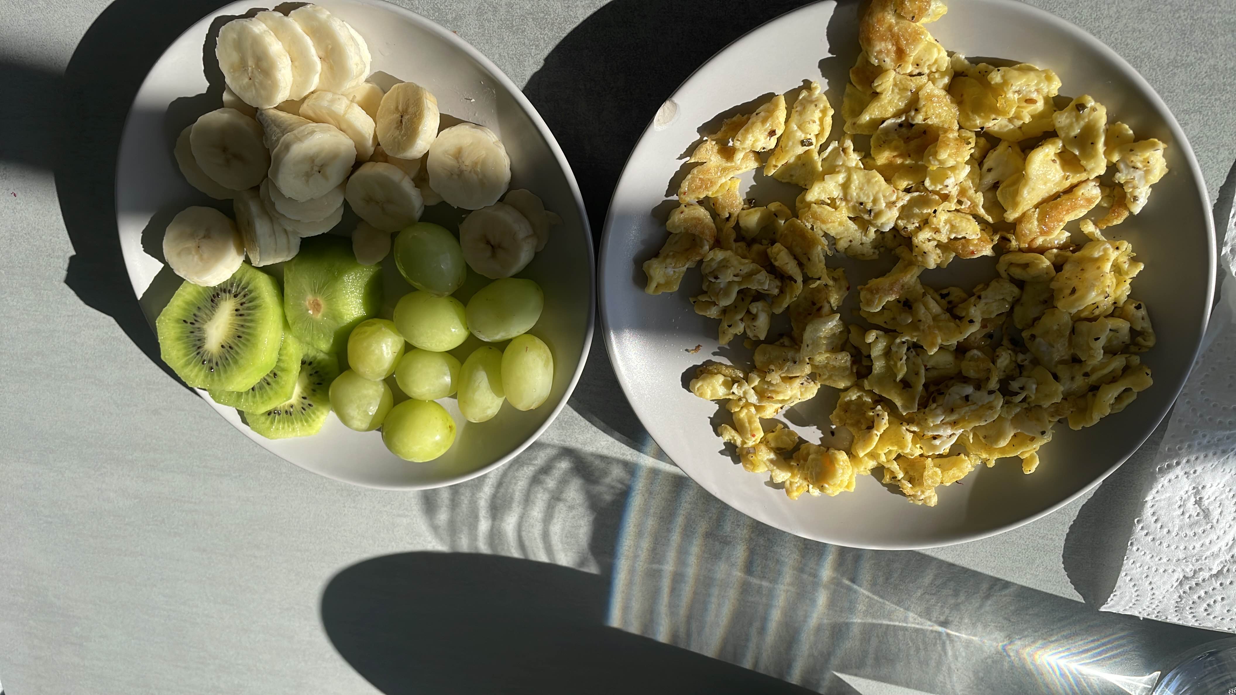 A balanced meal consisting of scrambled eggs, banana slices, kiwi slices, and green grapes, providing a mix of protein, carbs, and healthy fats.