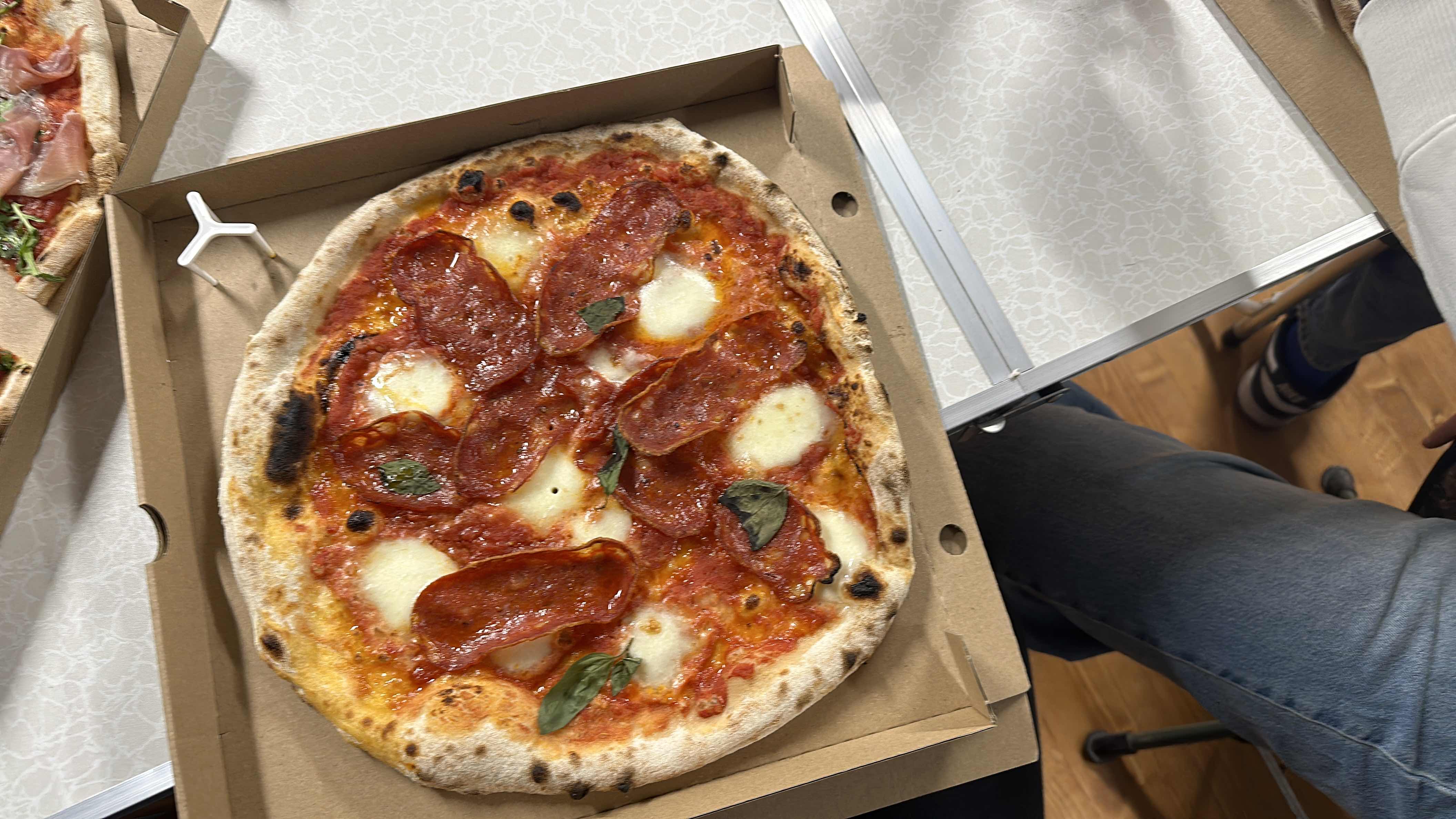 A pepperoni pizza with mozzarella cheese, tomato sauce, and fresh basil, served in a cardboard box.