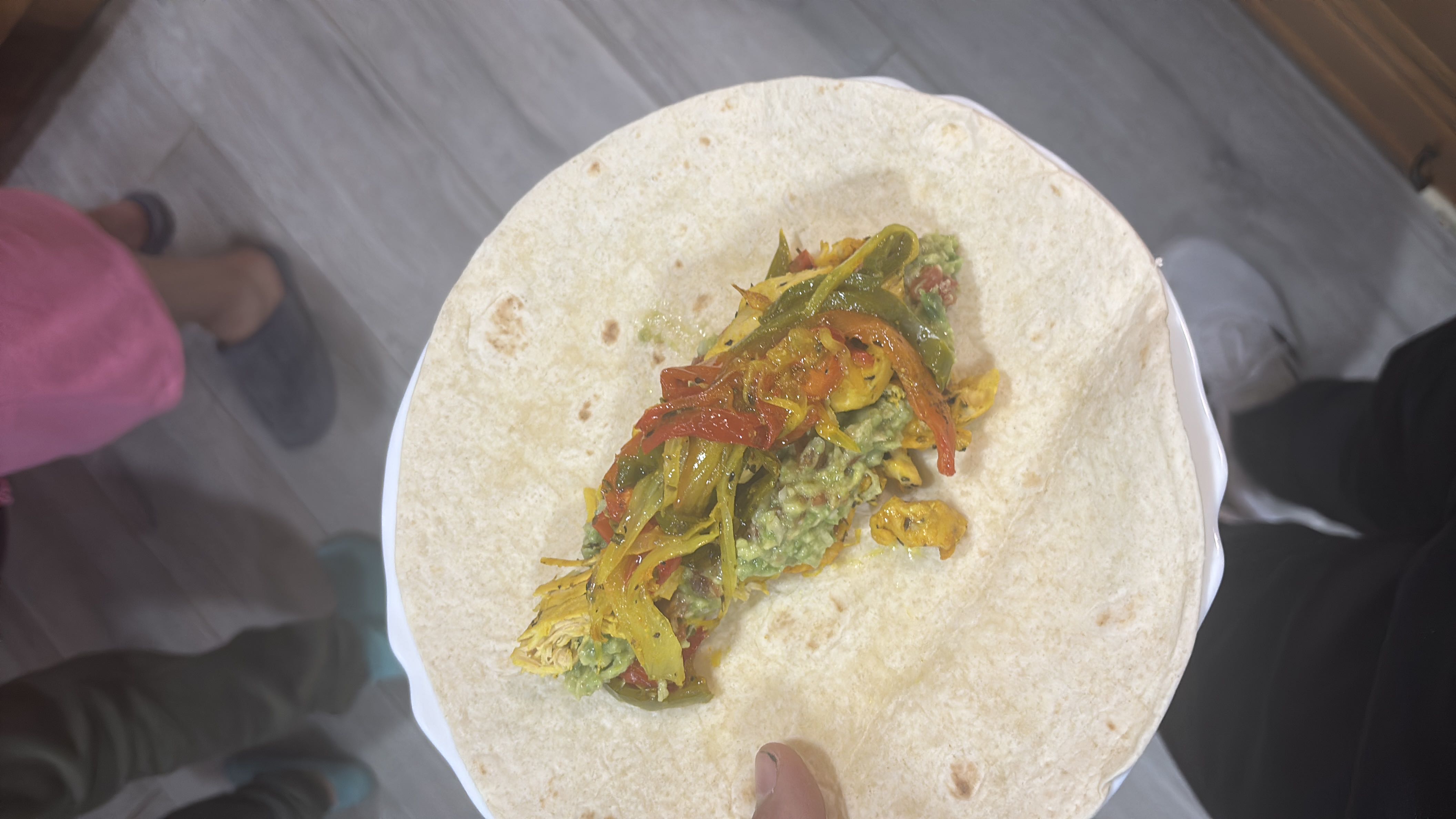 A tortilla wrap filled with chicken, guacamole, sautéed bell peppers, and onions, offering a balanced mix of protein, carbs, and fats.