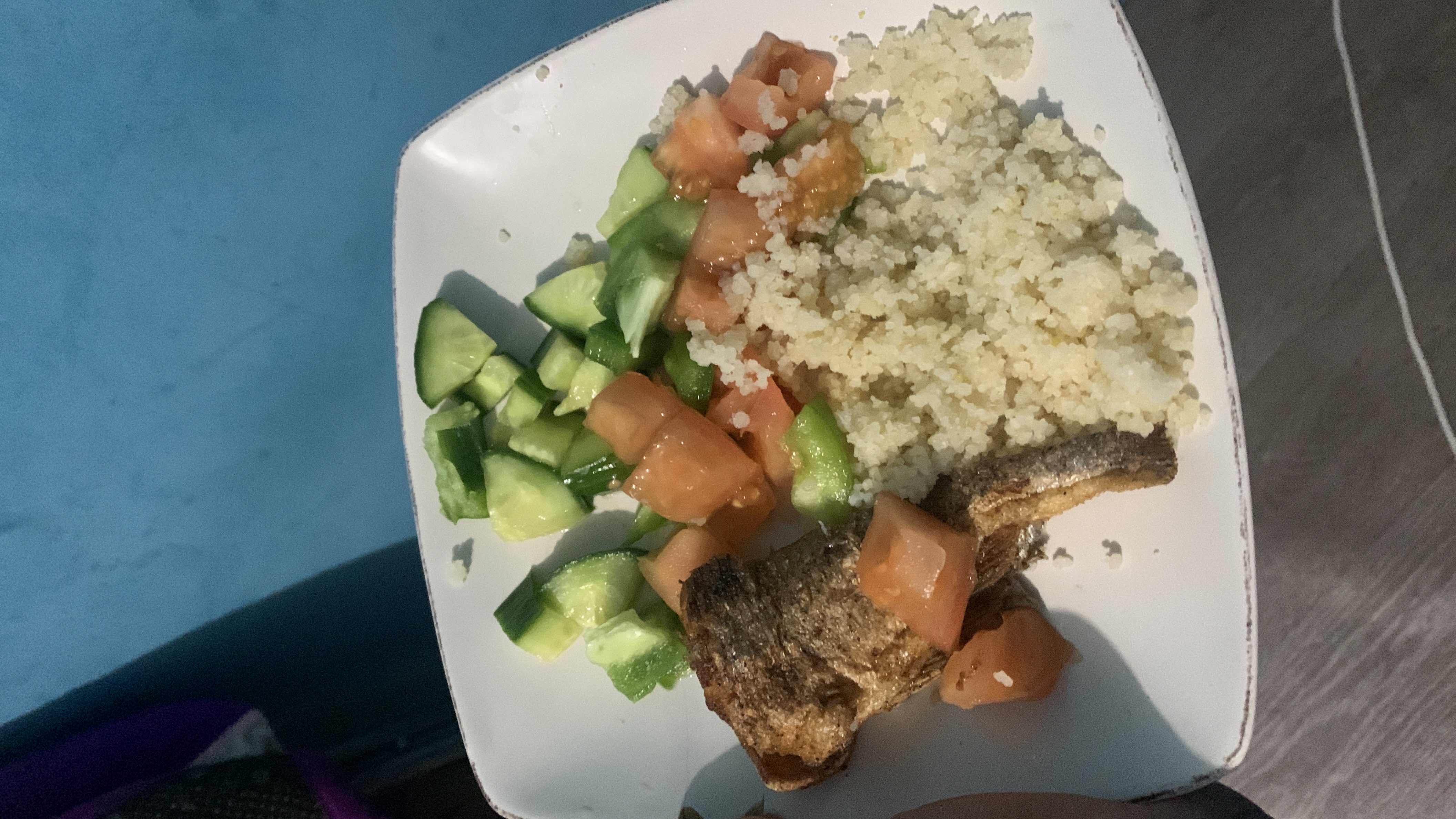 A balanced meal consisting of grilled fish, couscous, and a fresh salad of cucumber and tomato.