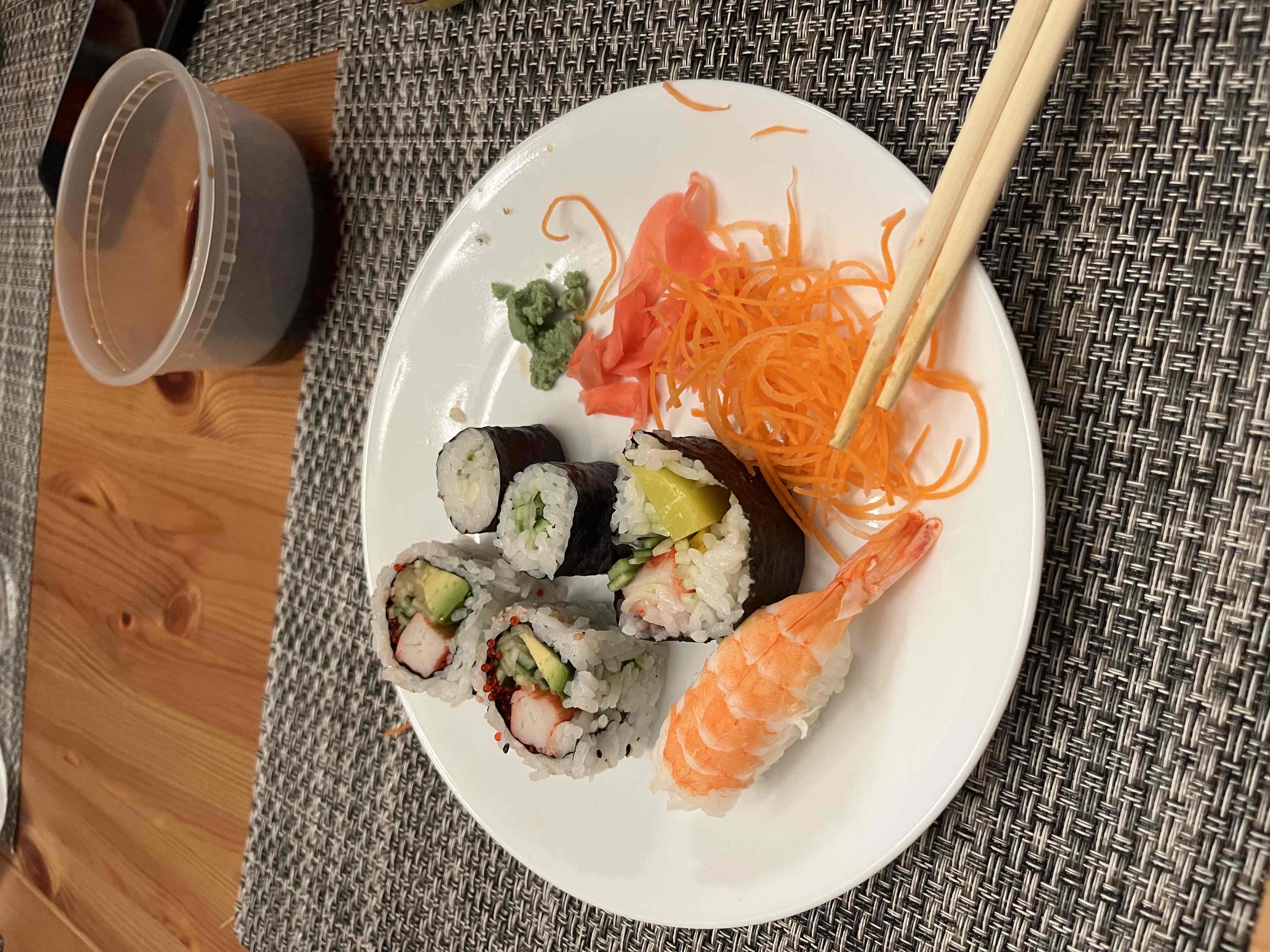A plate of sushi containing shrimp, crab stick, avocado, seaweed, and sushi rice, served with pickled ginger, wasabi, and shredded carrots.