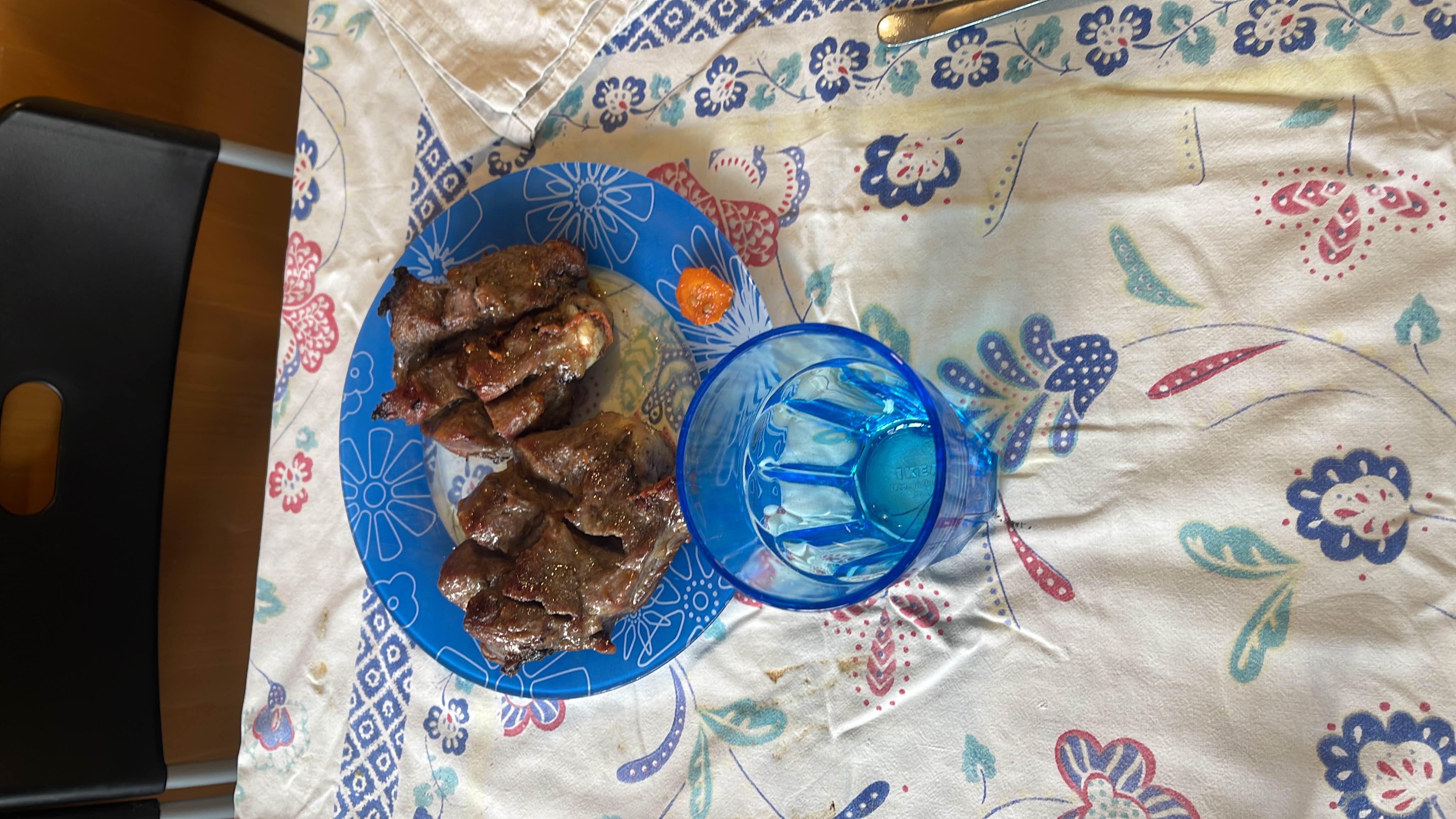A plate of grilled meat served on a blue plate, accompanied by a glass of water.