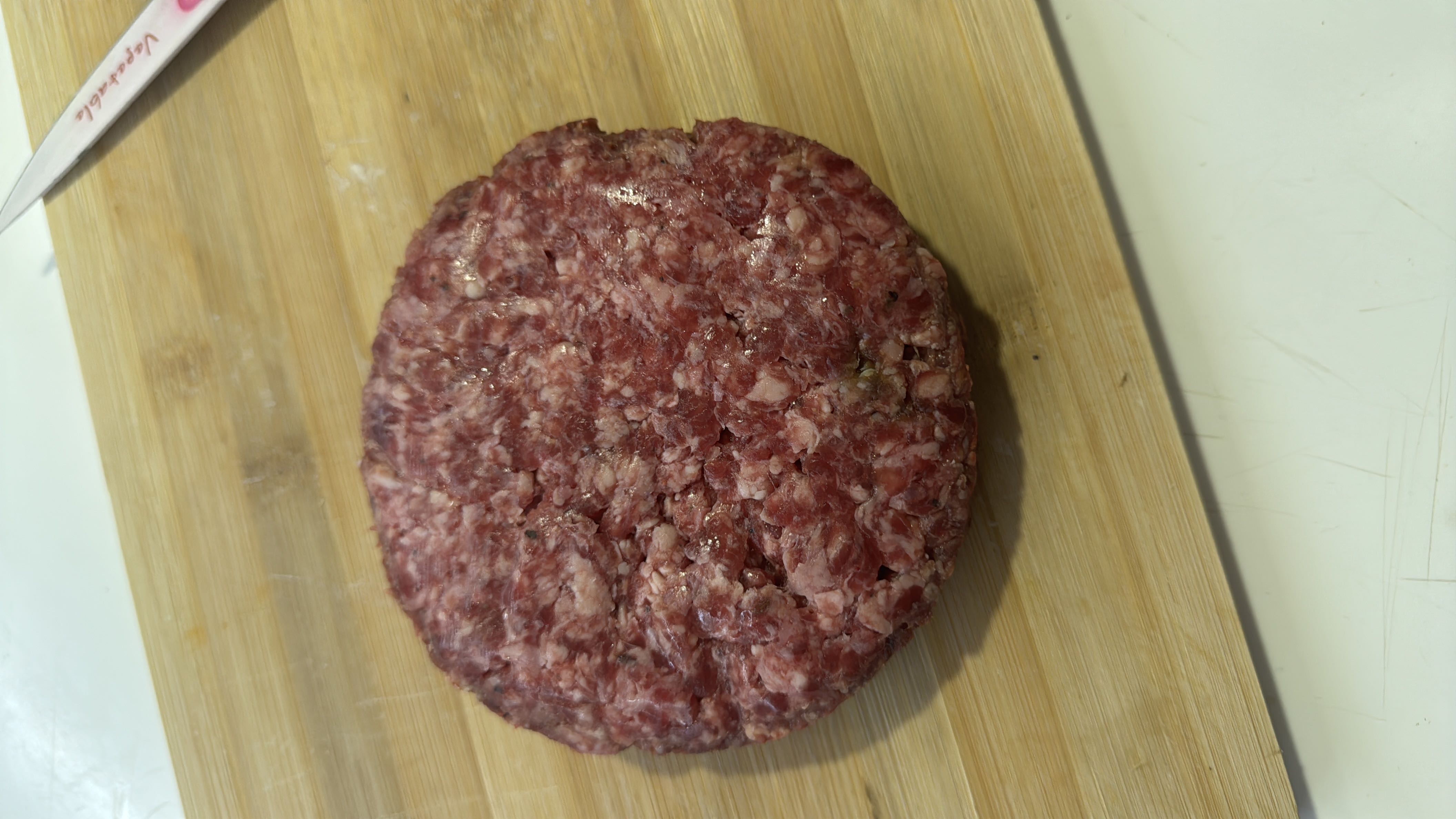 A raw ground beef patty, high in protein and fats, suitable for grilling or cooking.