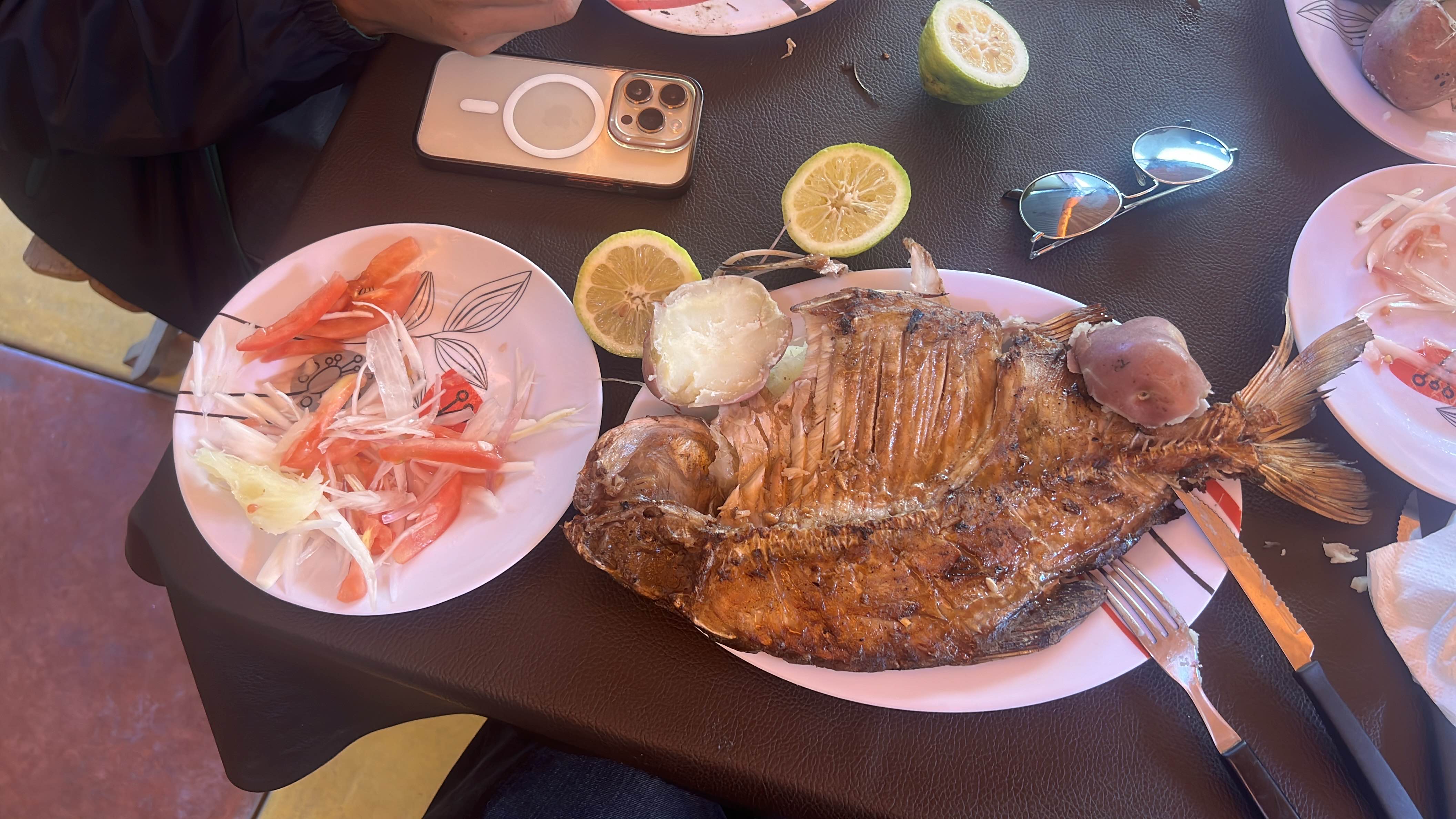 A meal consisting of grilled fish, boiled potato, and a fresh tomato and onion salad, served with lime slices.