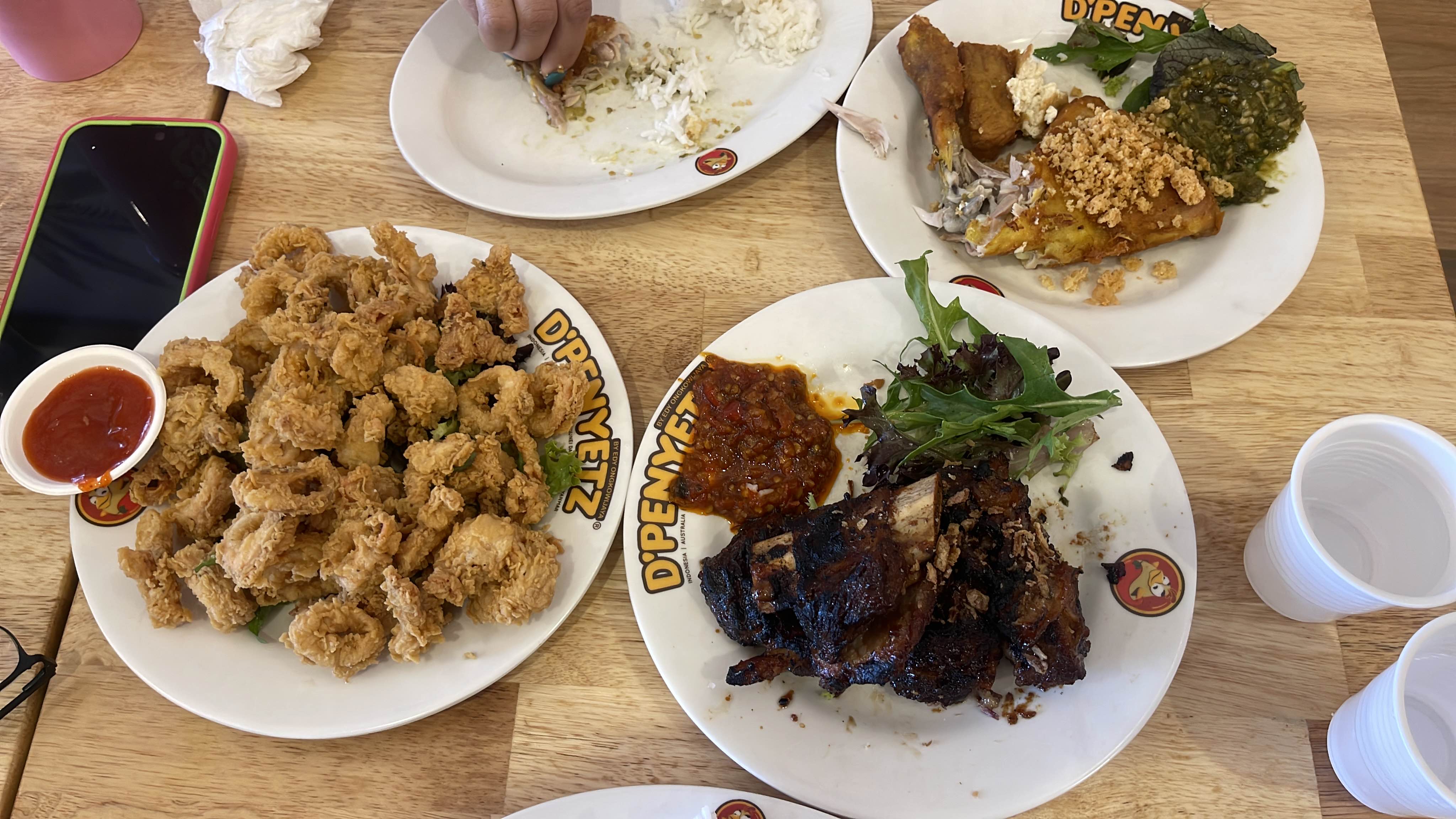 The image shows a variety of dishes including fried calamari, grilled ribs, and fried tofu with sambal, served with greens and sauces.