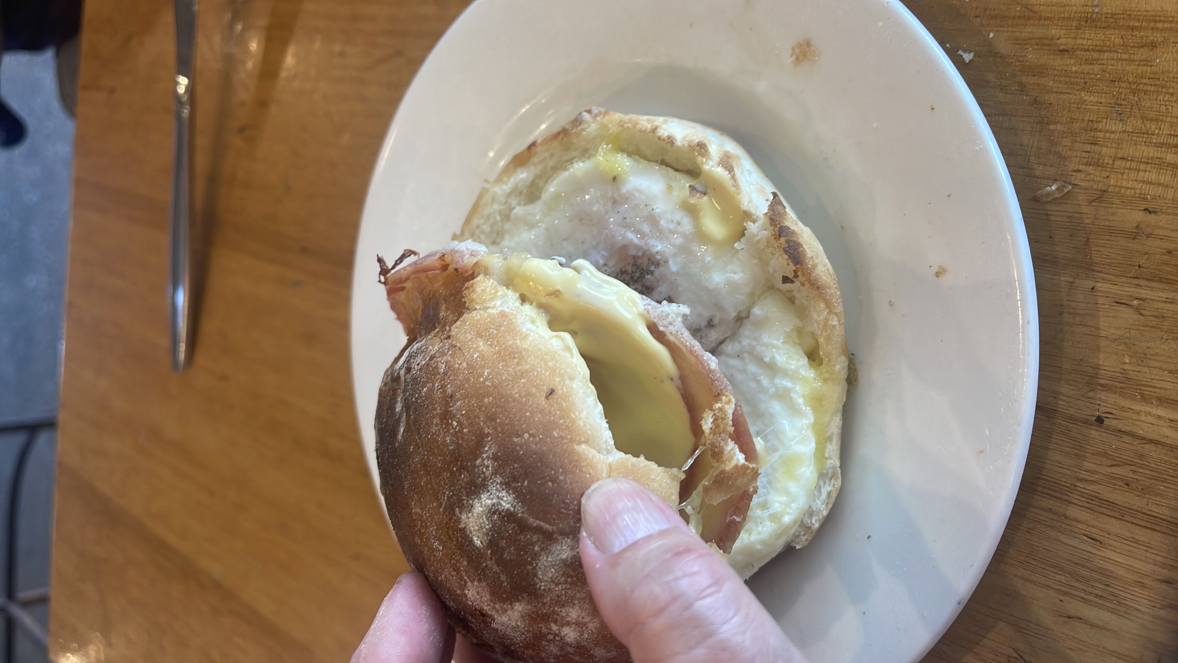 A breakfast sandwich consisting of a bread bun, fried egg, cheese, and ham.