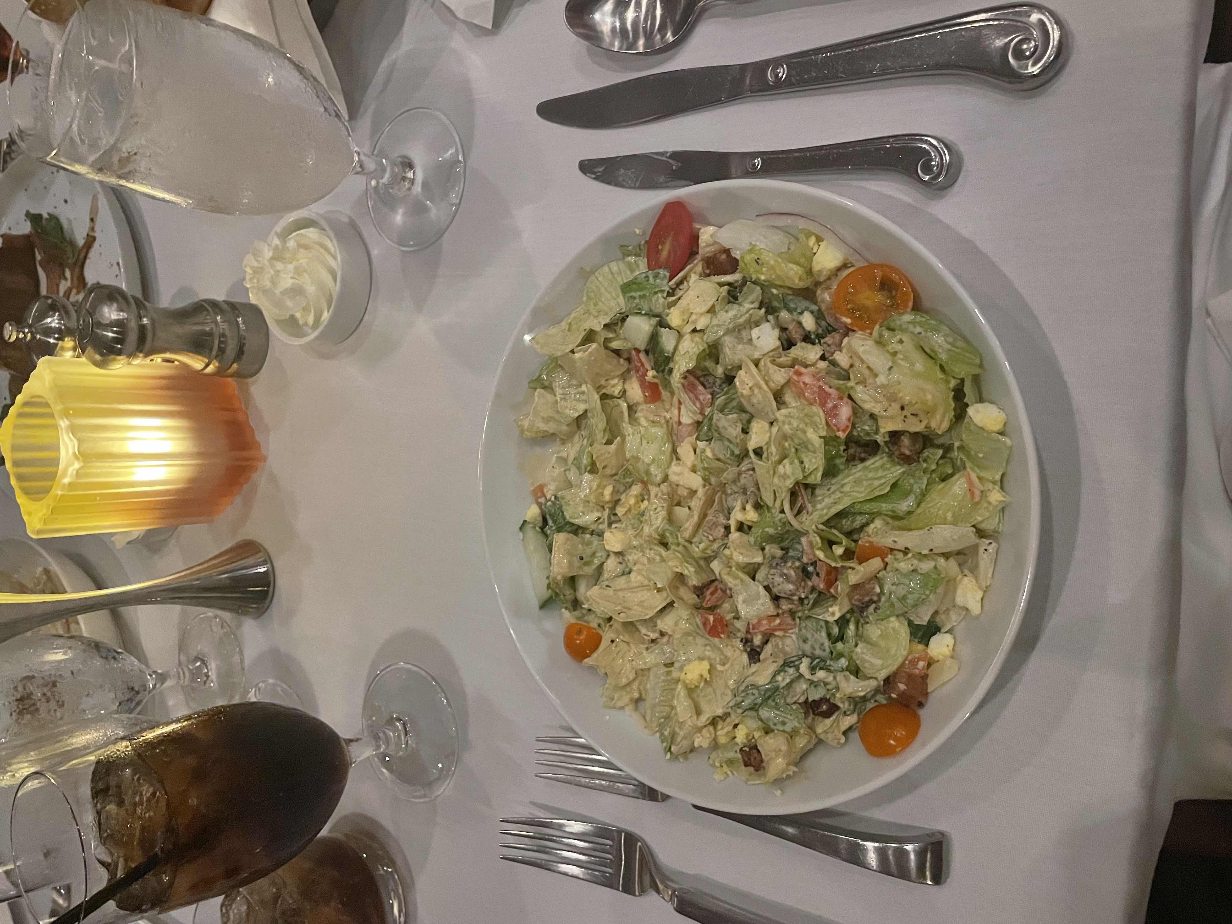 A fresh salad with lettuce, cherry tomatoes, boiled egg, bacon bits, cucumber, cheese, and dressing.